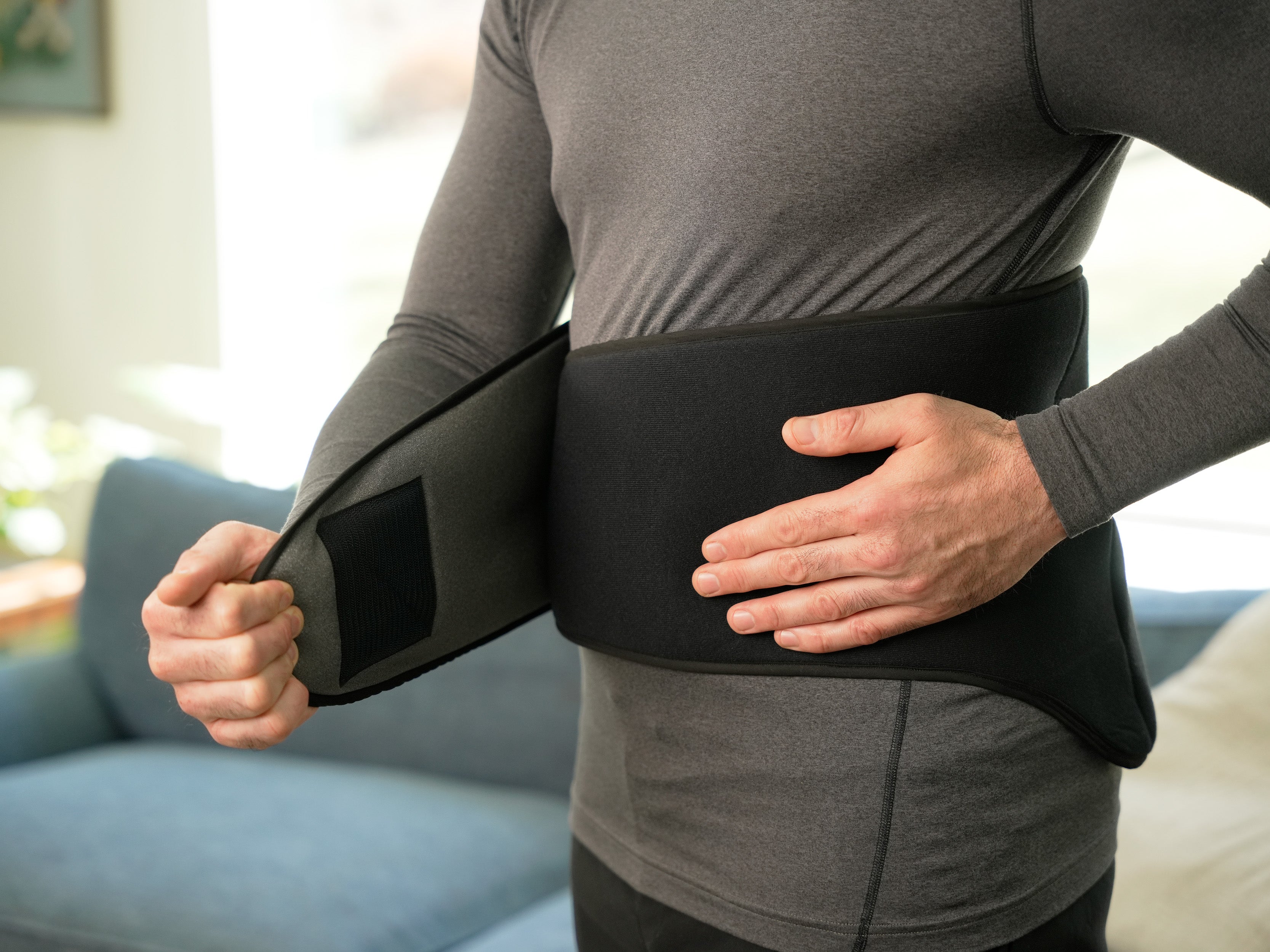 Person wearing a gray shirt and applying a Soft Ice® Lumbosacral Wrap on lower back.