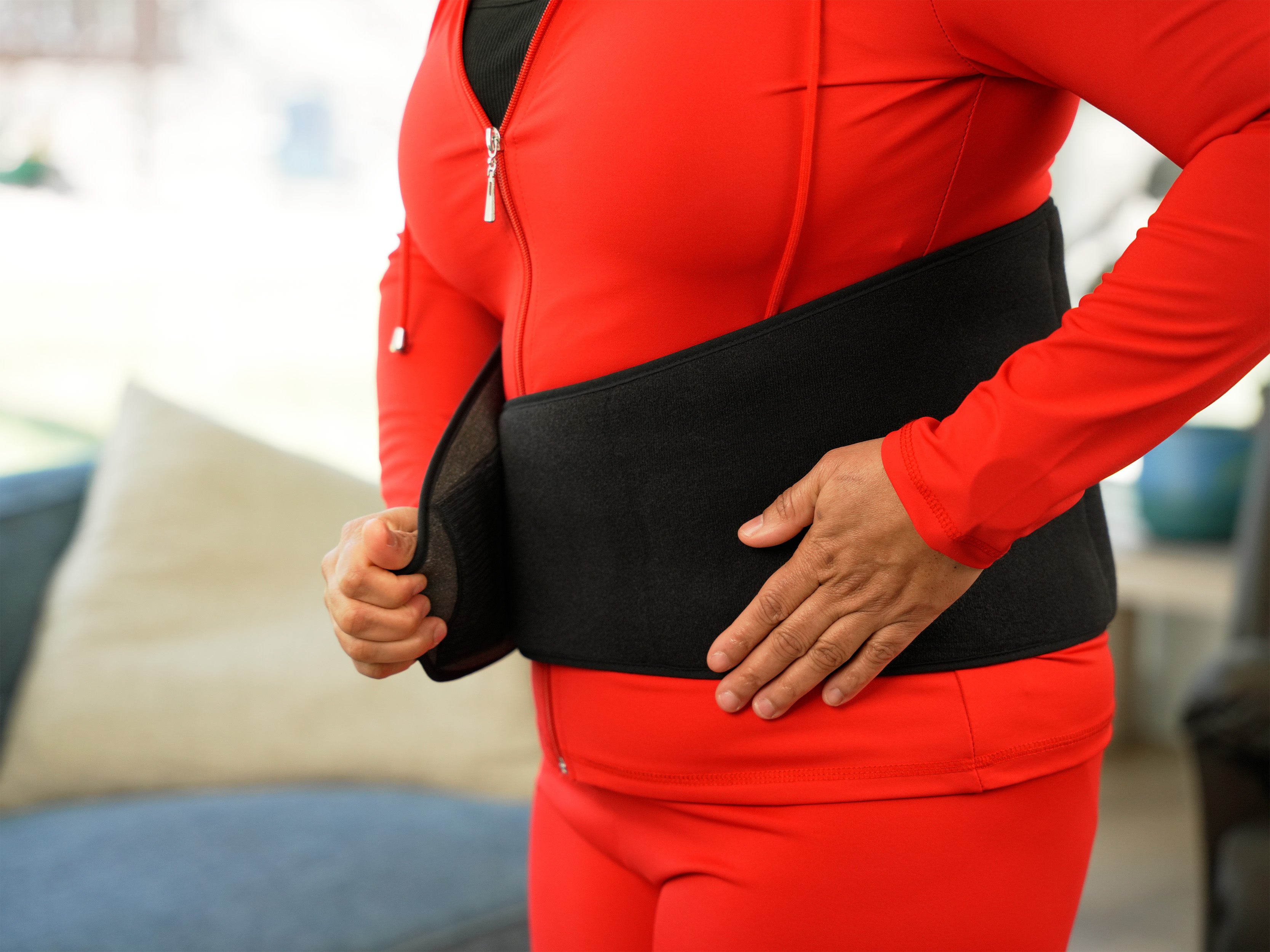 Woman applying a red outfit with a black Soft Ice® Back & Hip Wrap.