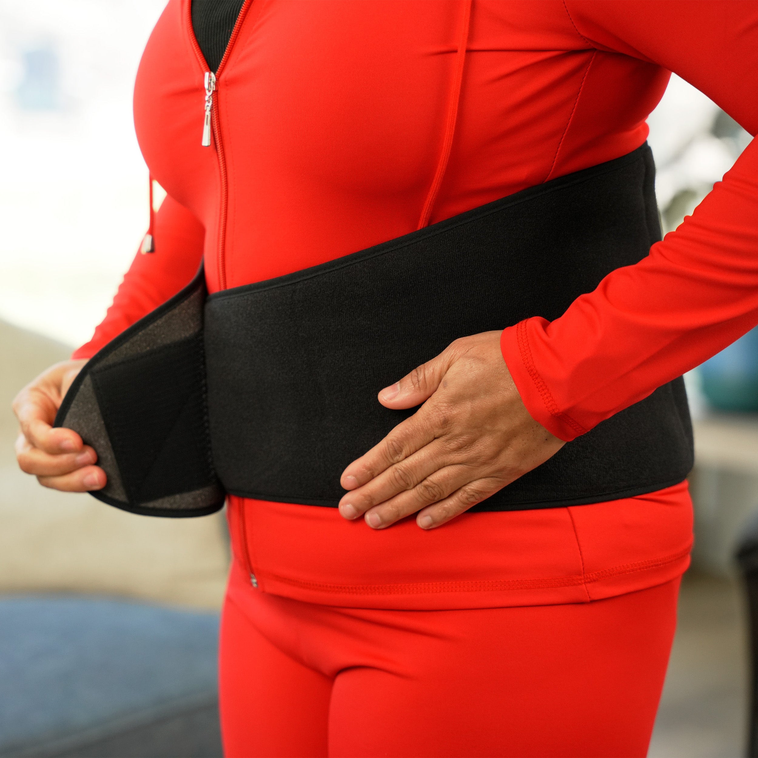Woman applying a red outfit with a black Soft Ice® Back & Hip Wrap.