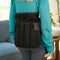 A woman viewed from behind wearing a black Moist Heat Thera-Temp Wrap worn over her teal long-sleeve top in a living room setting.