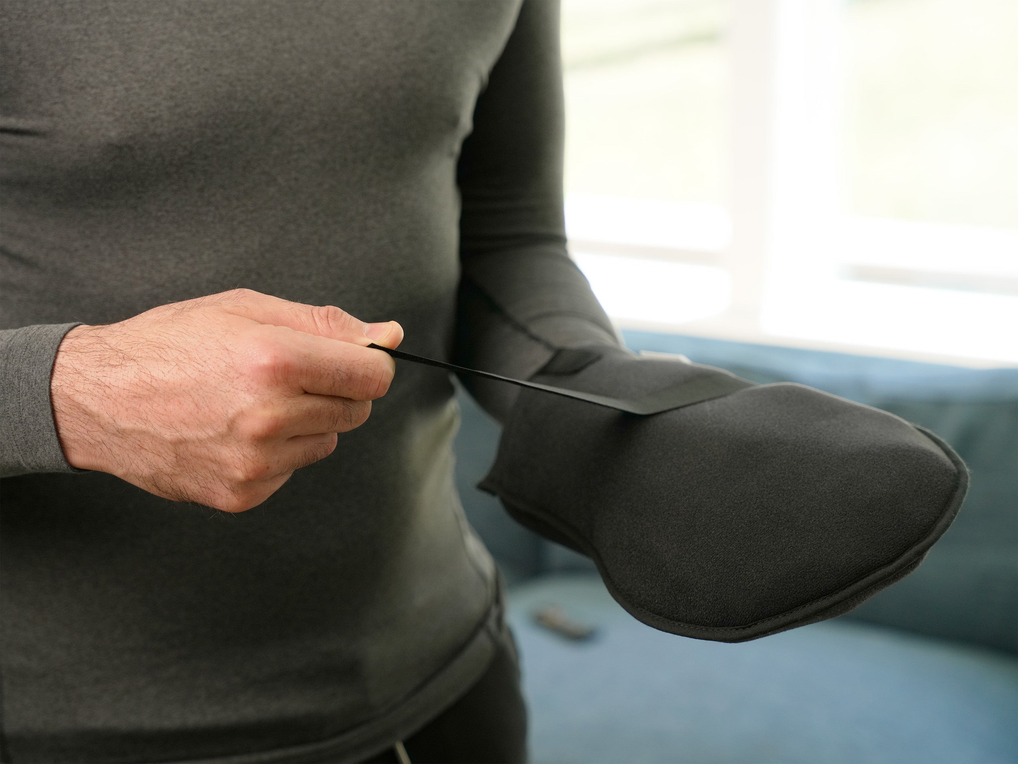 Man wearing a gray long-sleeve shirt applying a black Soft Ice® Mitt on his hand in a home setting.