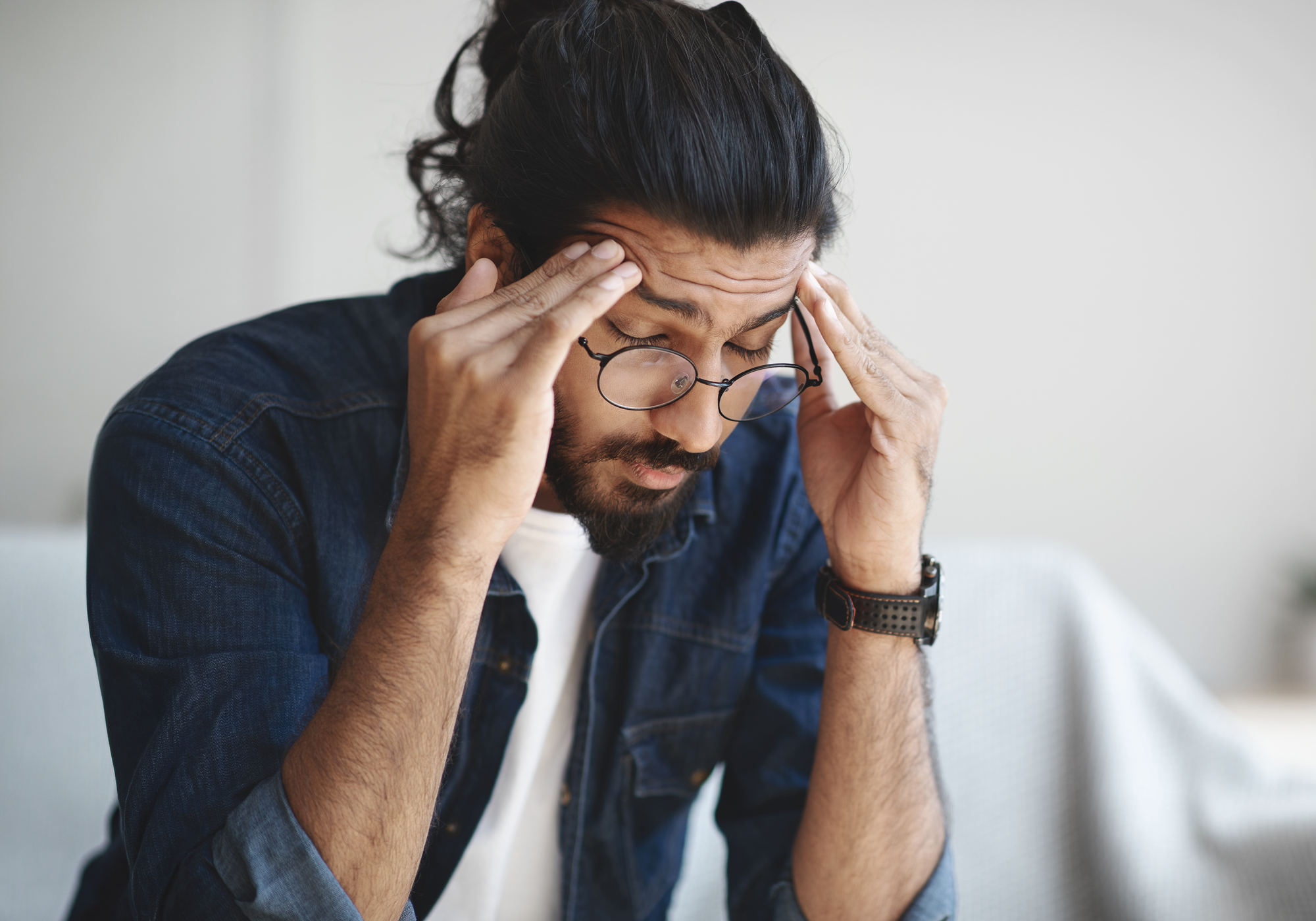 Man with glasses holding his head in apparent stress or pain