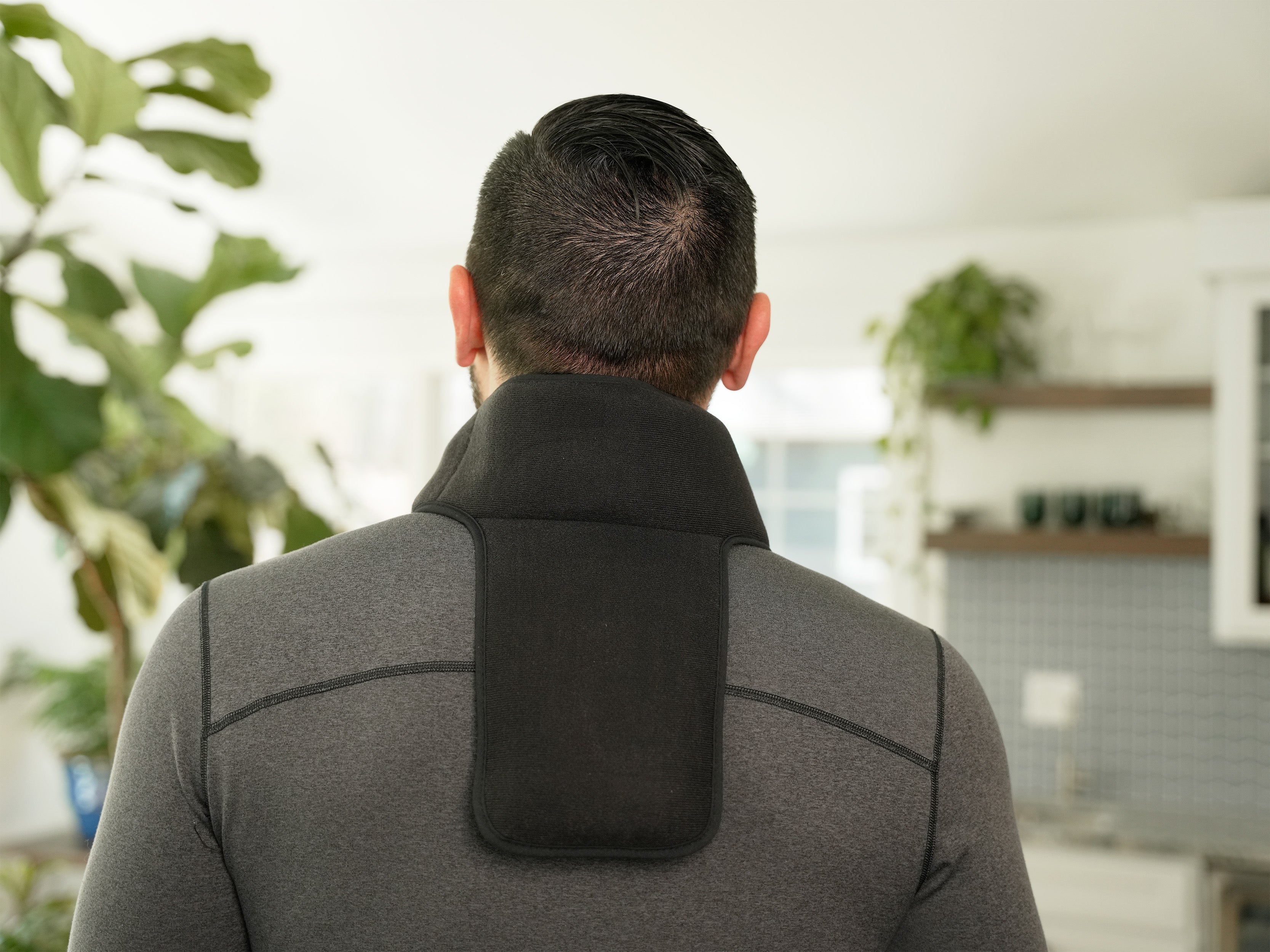 Man wearing a black Soft Ice® Neck & Upper Spine Wrap in a living room setting