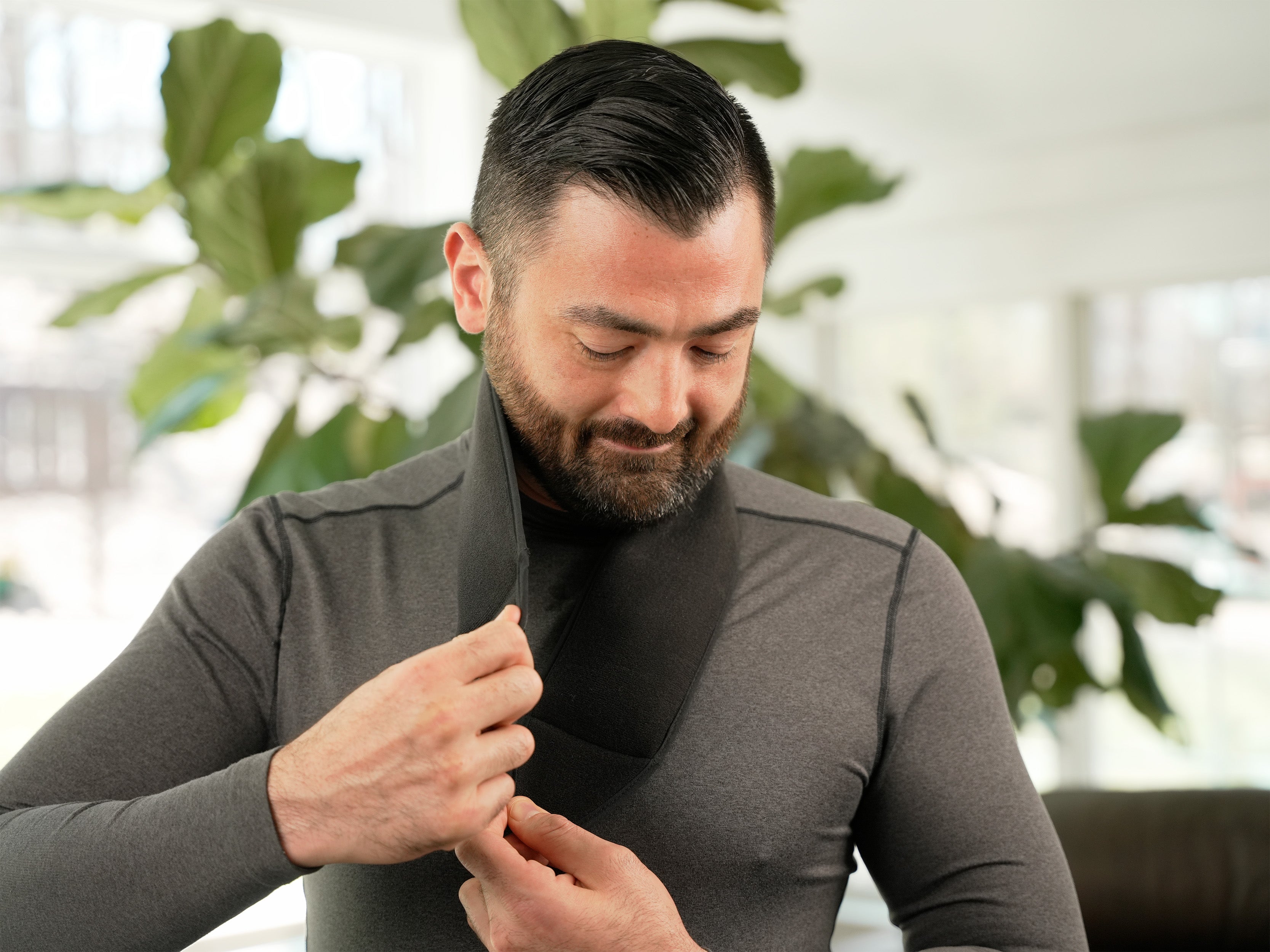 Man applying the black Soft Ice® Neck and Head Wrap on his neck in a living room setting.