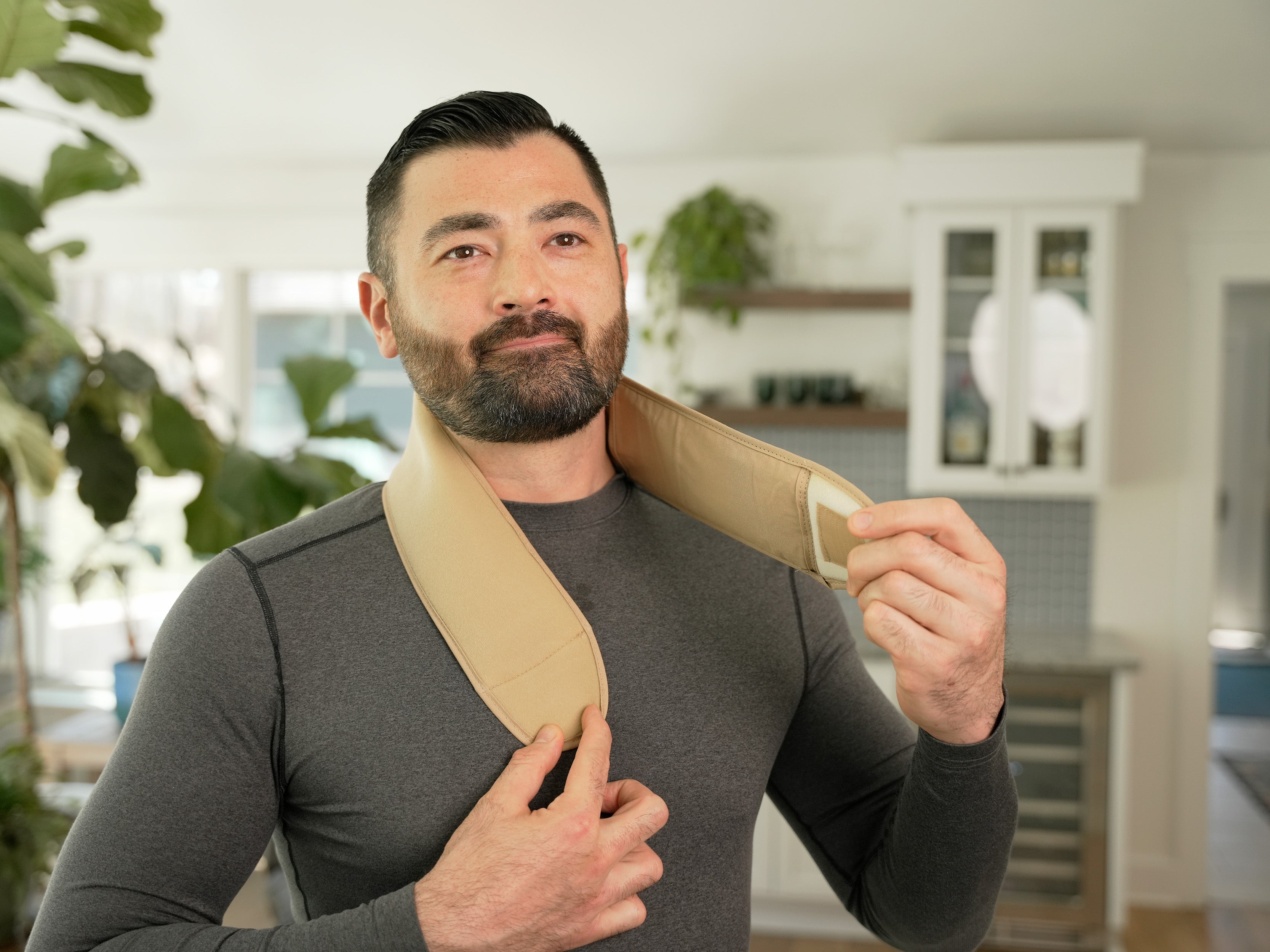 Man applying the Khaki Soft Ice® Neck and Head Wrap on his neck in a living room setting.