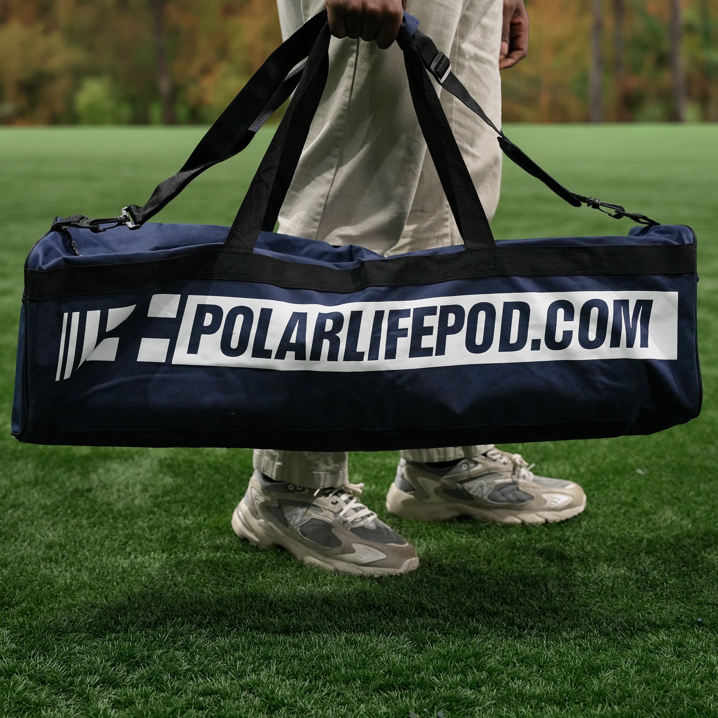 Person holding the portable Polar Life Pod® in it's navy blue carrying bag with 'PolarLifePod.com' on a grassy field.