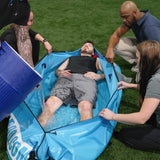 Person with heat illness laying in portable Polar Life Pod® with people holding it open and pouring in ice-water from 10 gallon container.