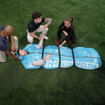 People assisting a person lying in the blue portable Polar Life Pod® on a grassy field.