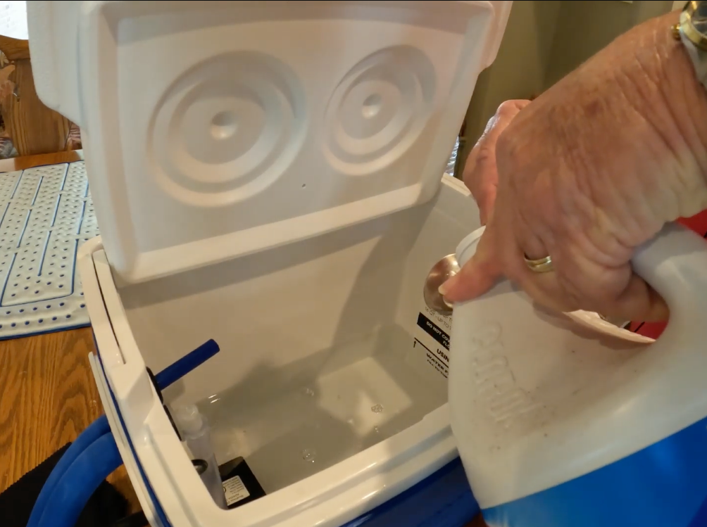 A close-up of a person's hand pouring liquid from a white and blue plastic jug into an Active Ice® Cold Therapy System.