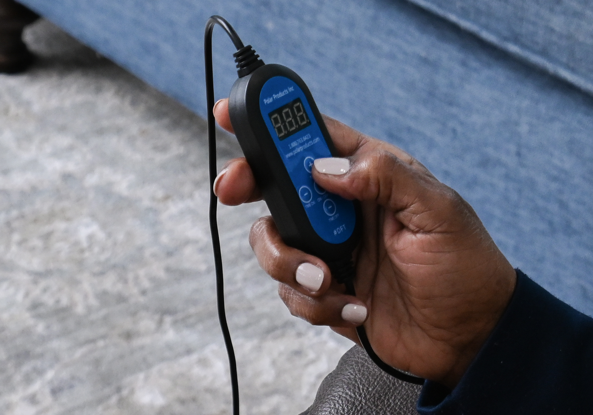 Hand holding a digital timer with a blue display, sitting on a couch.