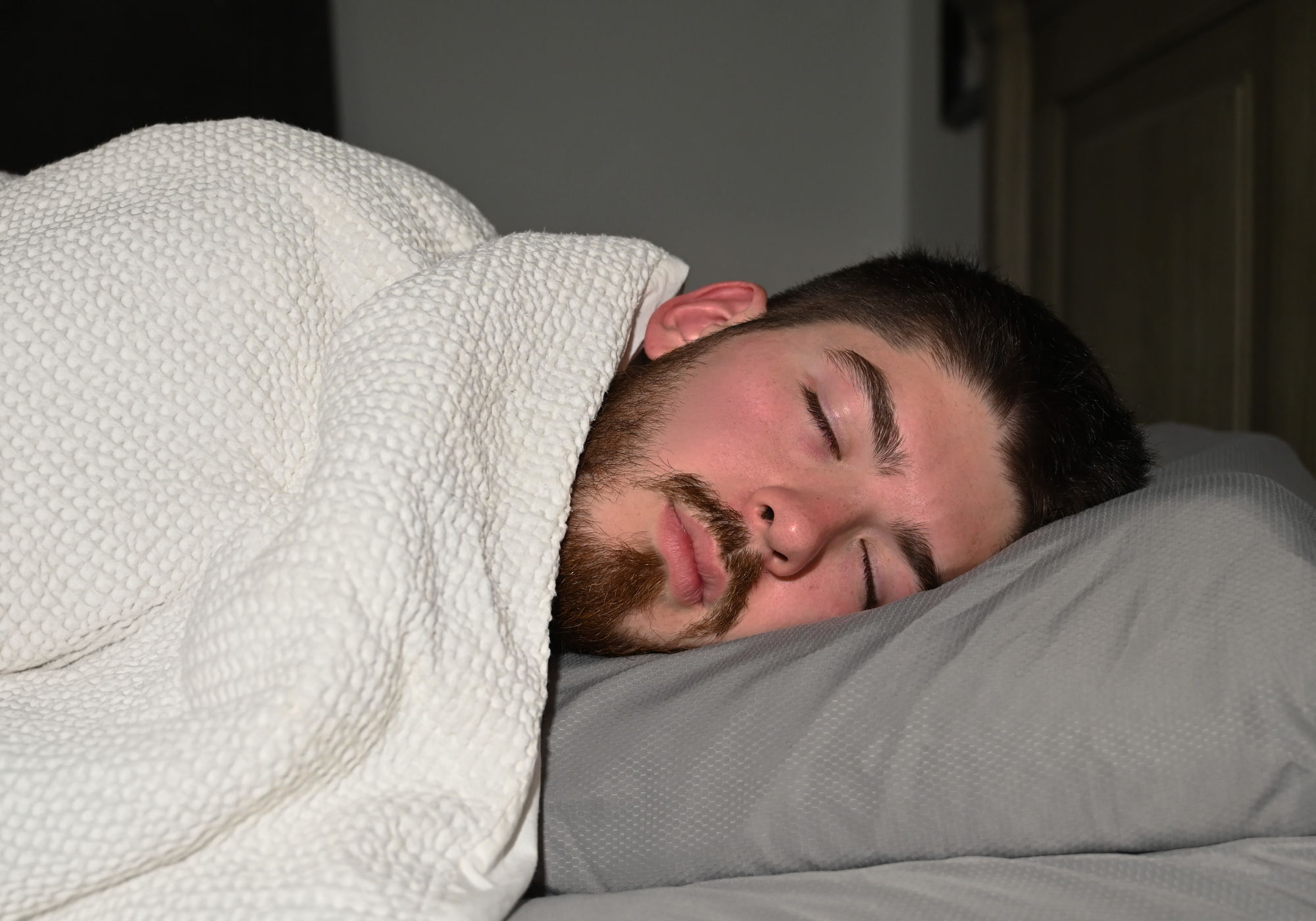 Man sleeping peacefully under a white blanket on a pillow.