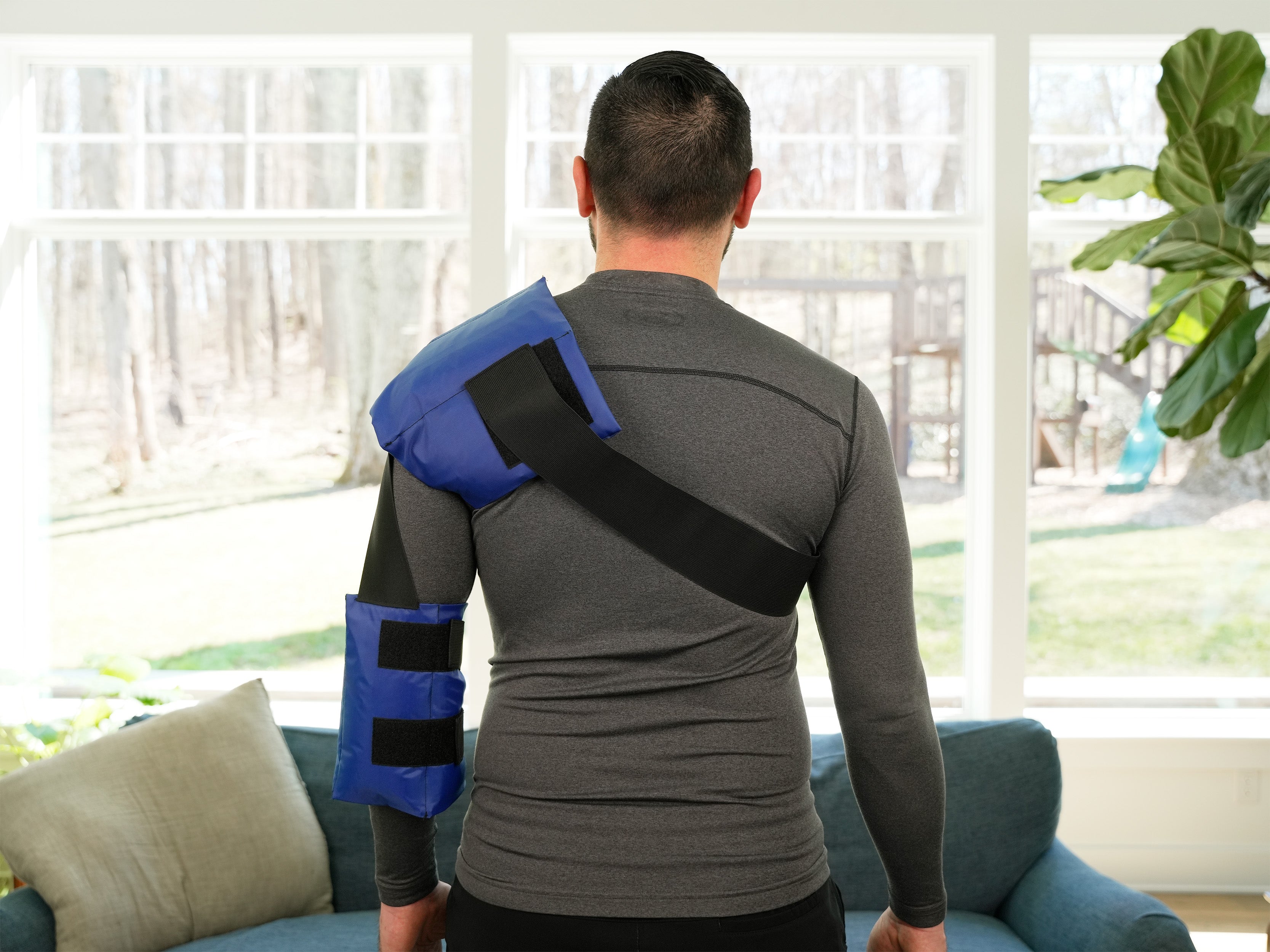 Man wearing a blue and black Soft Ice® Shoulder and Elbow Wrap in a living room.