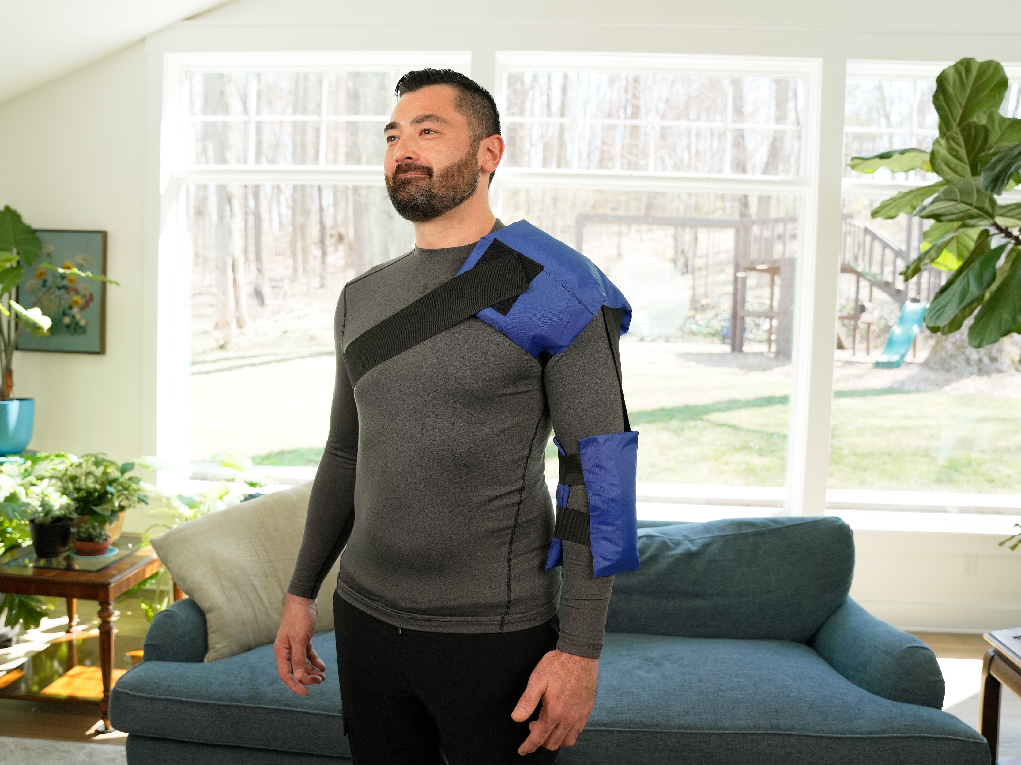 Man wearing a blue and black Soft Ice® Shoulder and Elbow Wrap in a living room.