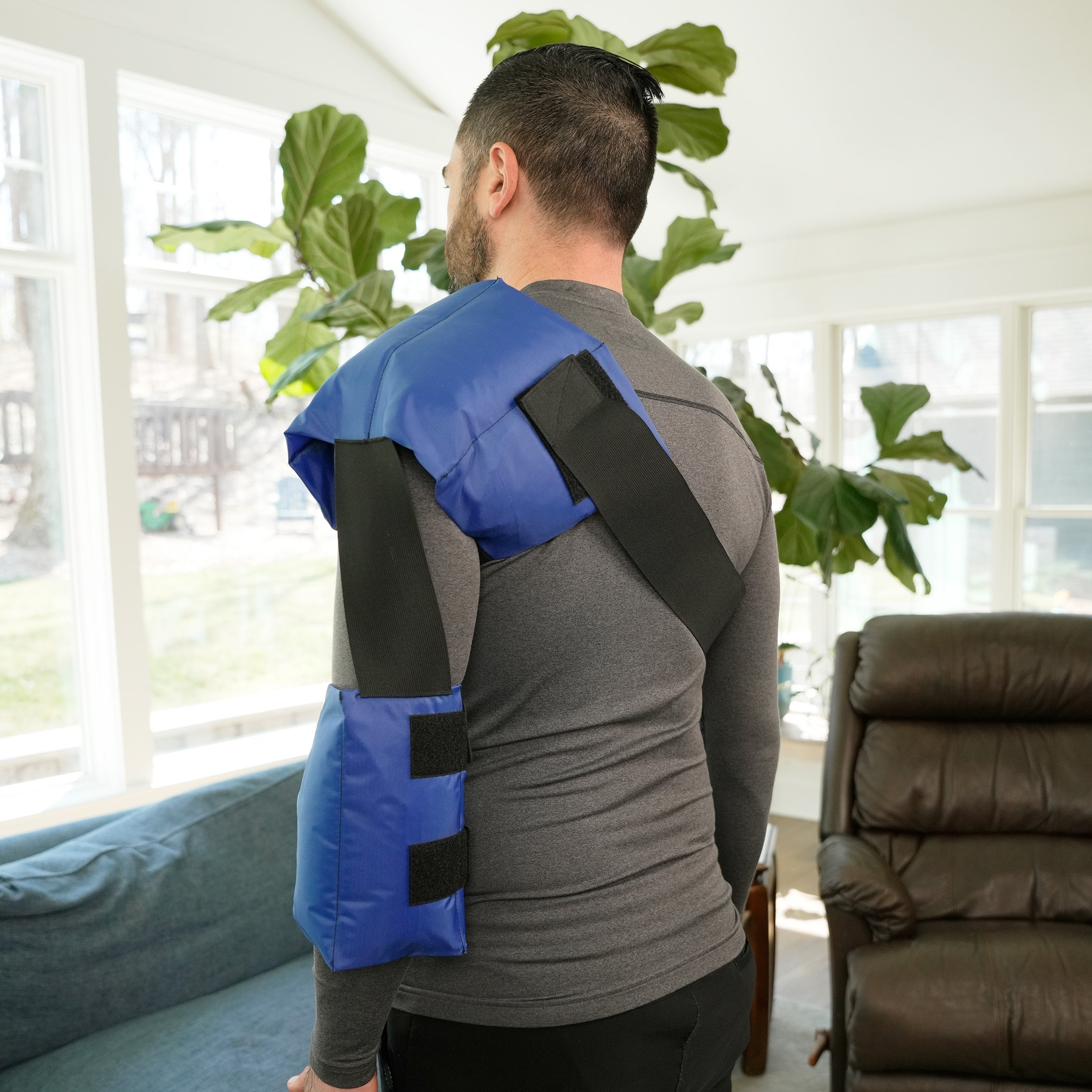 Man wearing a blue and black Soft Ice® Shoulder and Elbow Wrap in a living room.