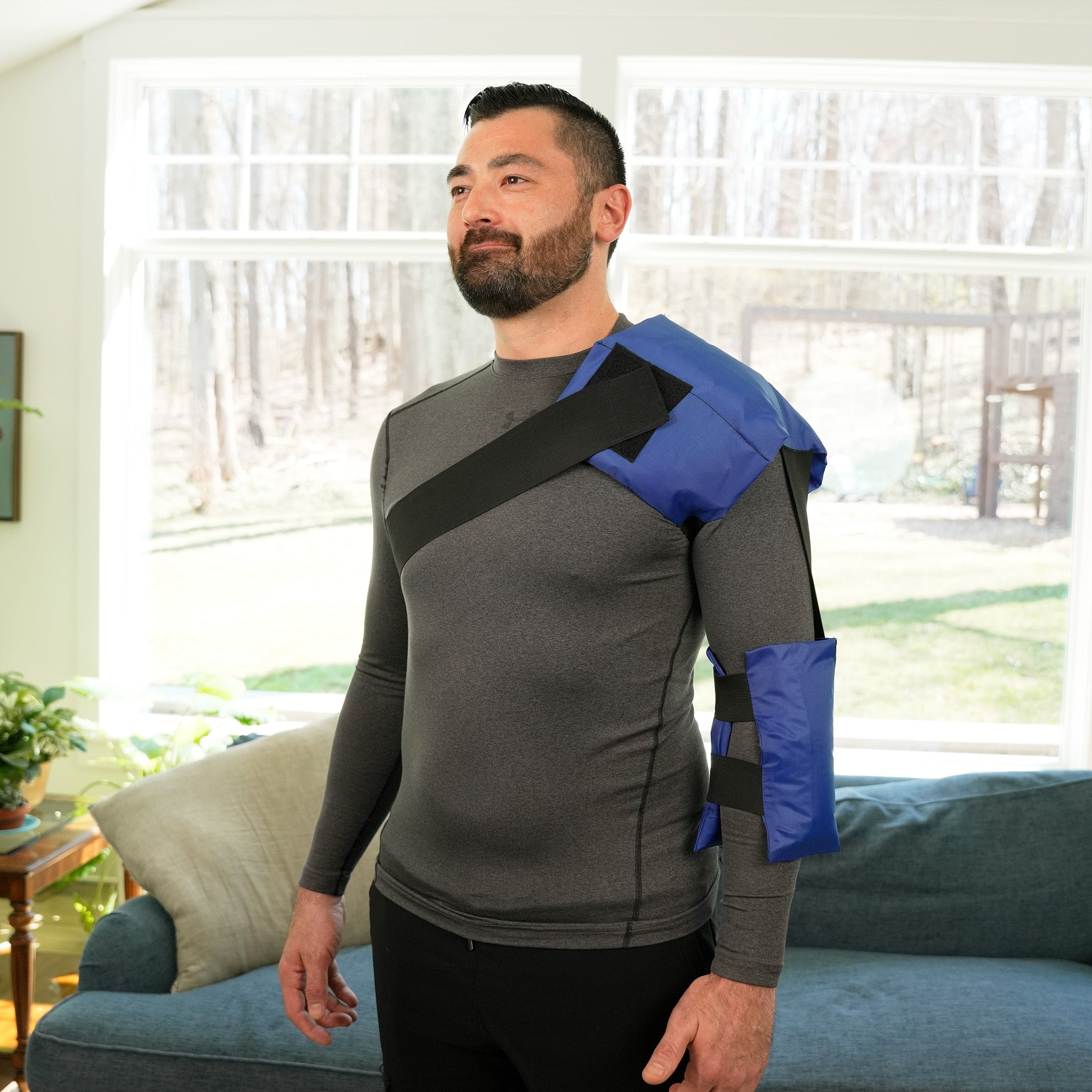 Man wearing a blue and black Soft Ice® Shoulder and Elbow Wrap in a living room.
