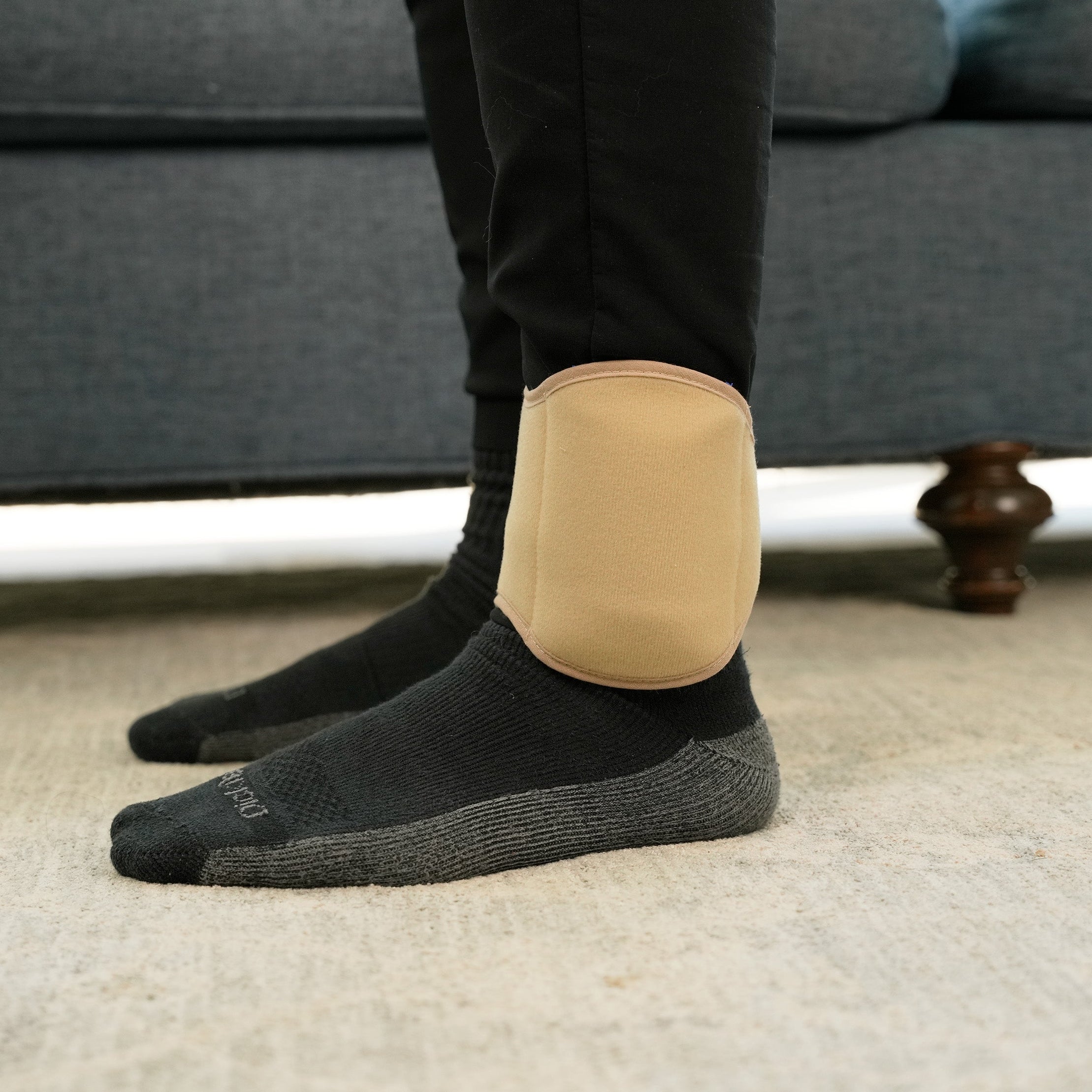 Person wearing black socks with a Khaki Soft Ice® Ankle Wrap in a living room setting.