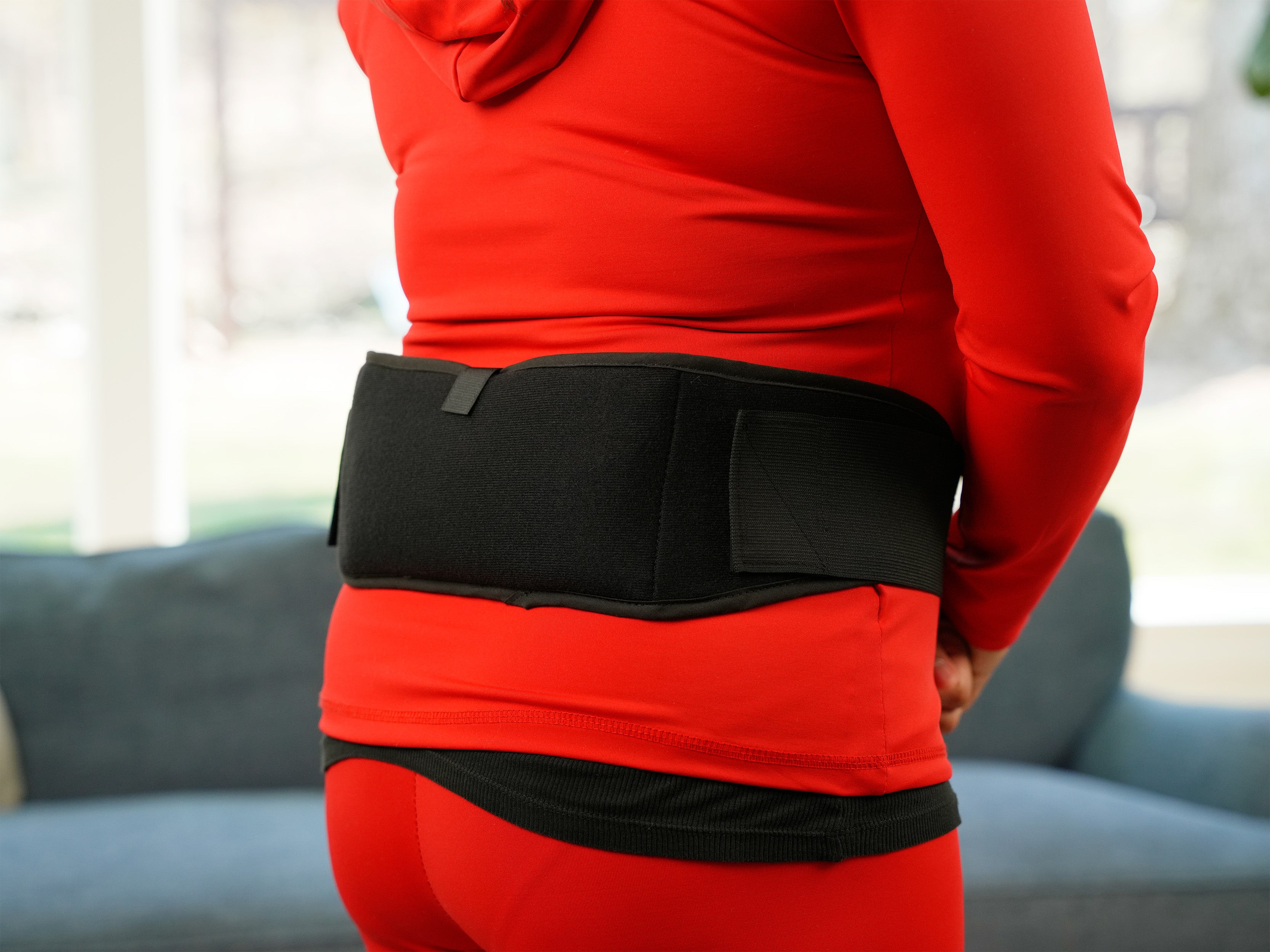 Person wearing a red outfit with a black Soft Ice® Standard Universal Compression Wrap on their back in an indoor setting.
