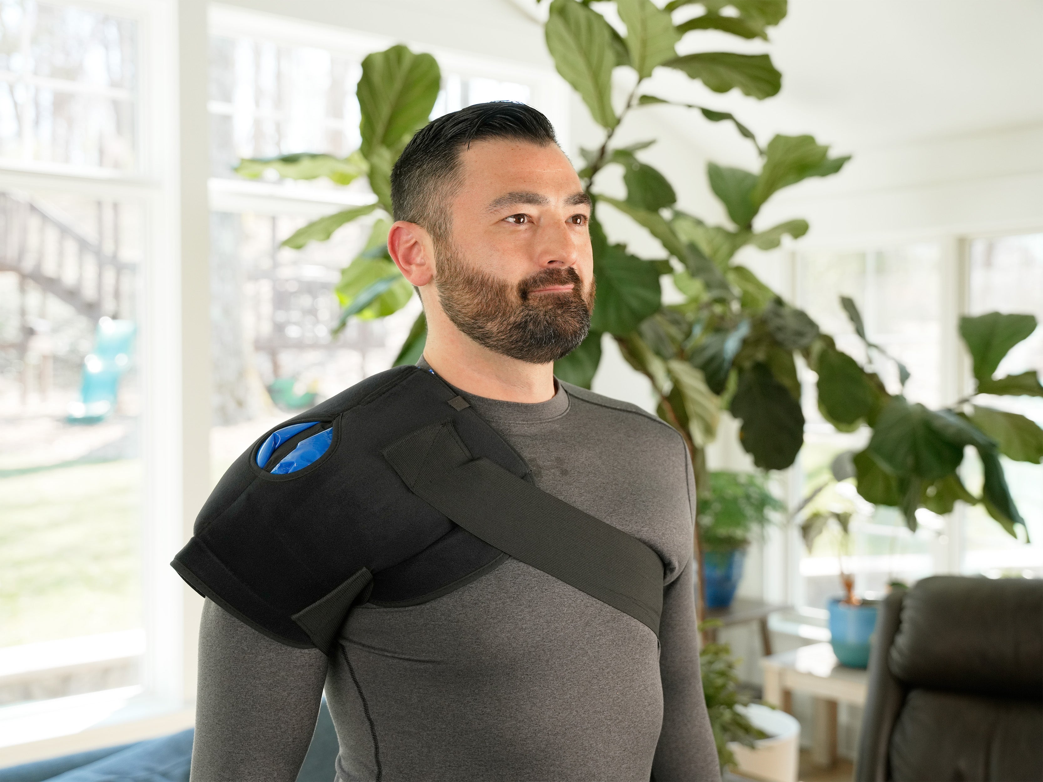 Man wearing a black Soft Ice® Shoulder Wrap in a room with plants