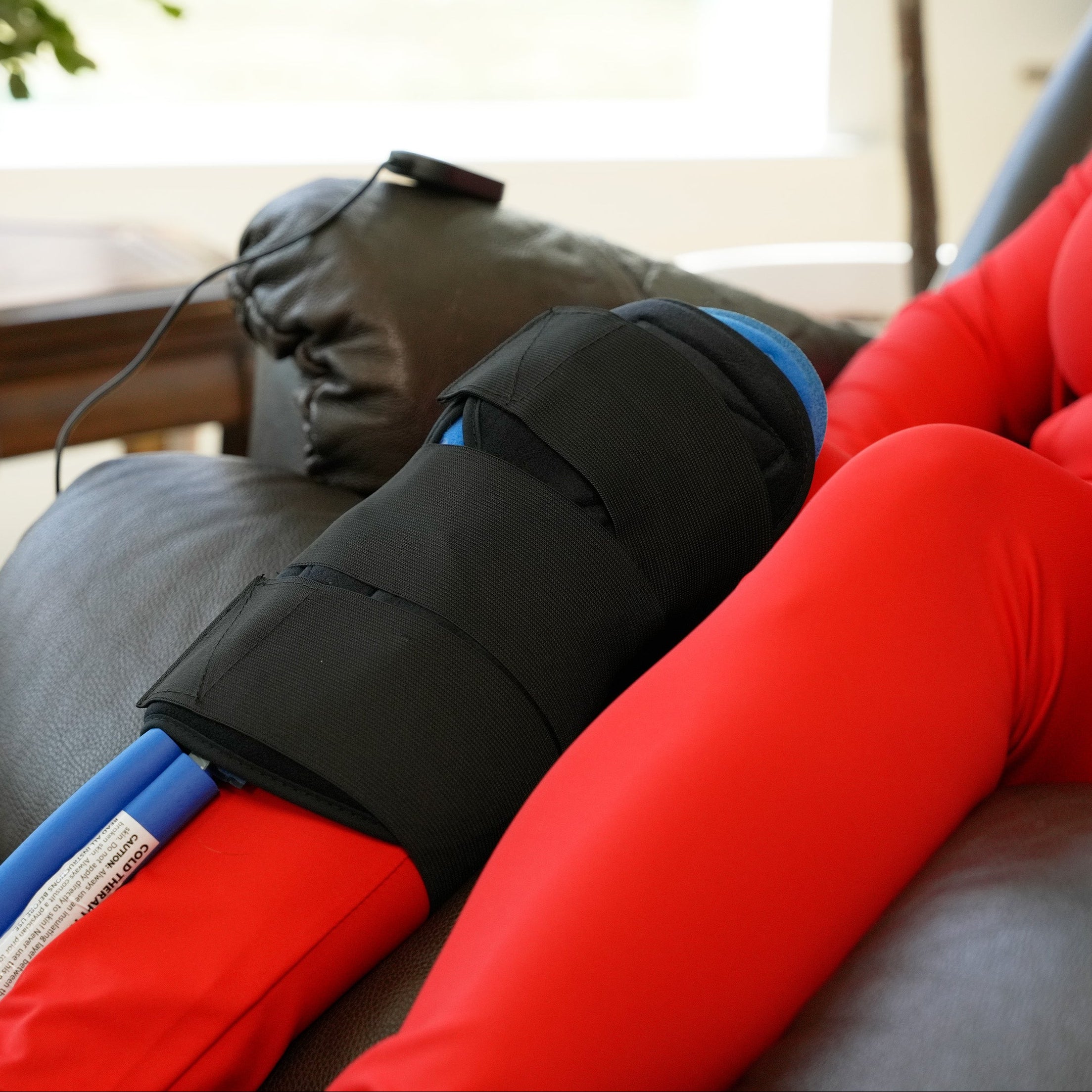 Woman in a recliner using a Active Ice® 3.0 Knee & Joint Compression Wrap on her knee.