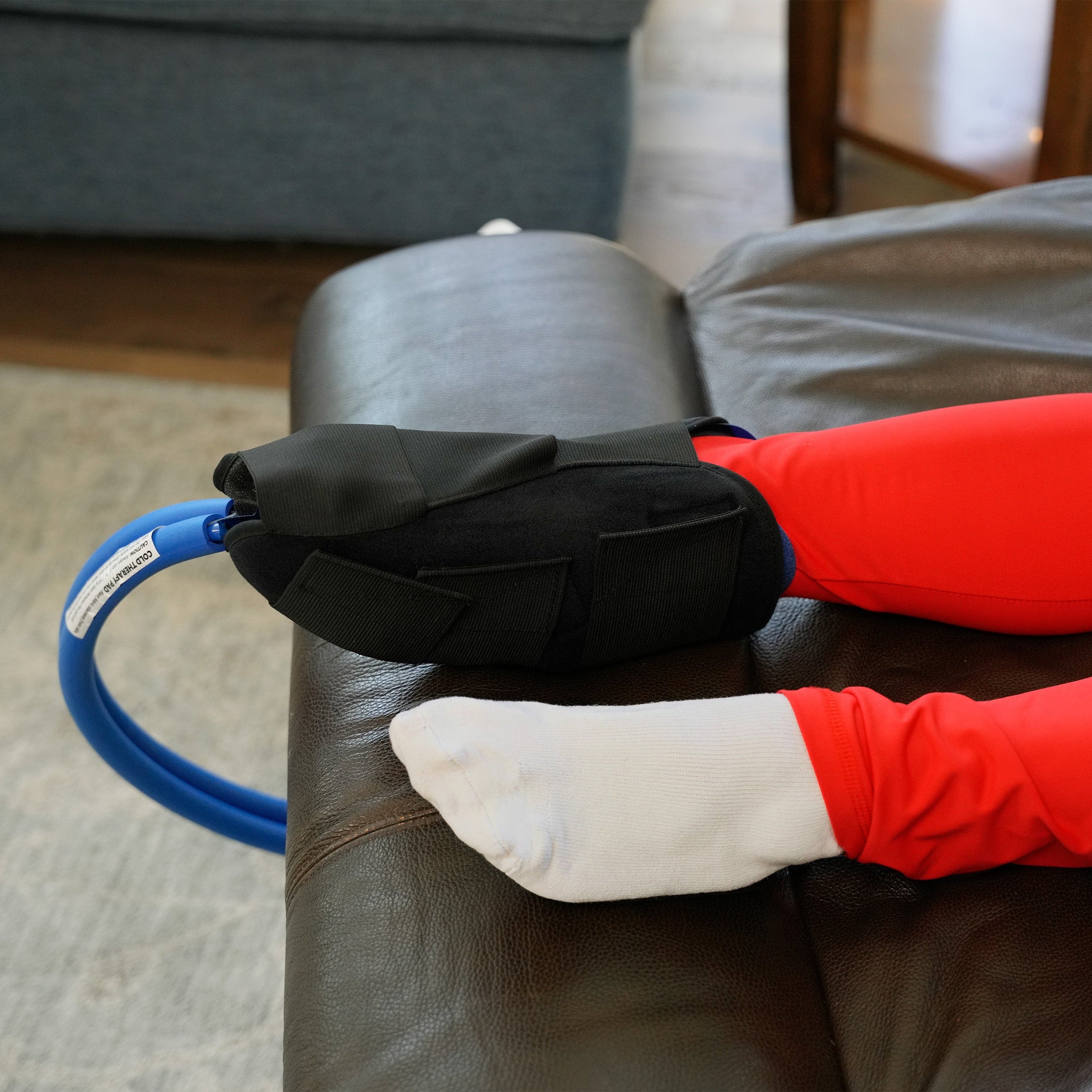 Woman in a recliner with red leggings wearing a Woman in a recliner using a Active Ice® 3.0 Knee & Joint Compression Wrap on her foot and ankle.