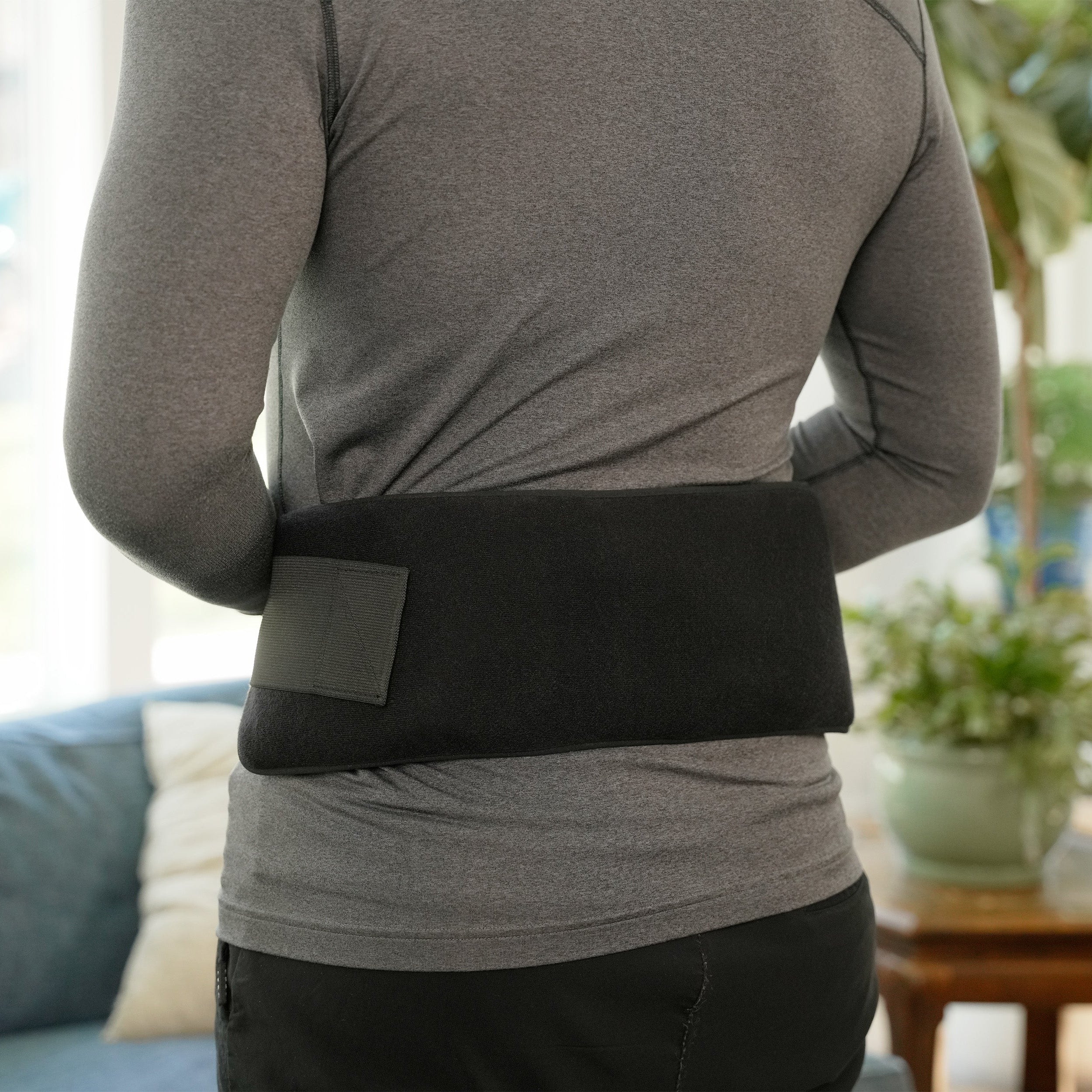 Person wearing a black Soft Ice® Double Universal Compression Wrap on the back in a living room setting