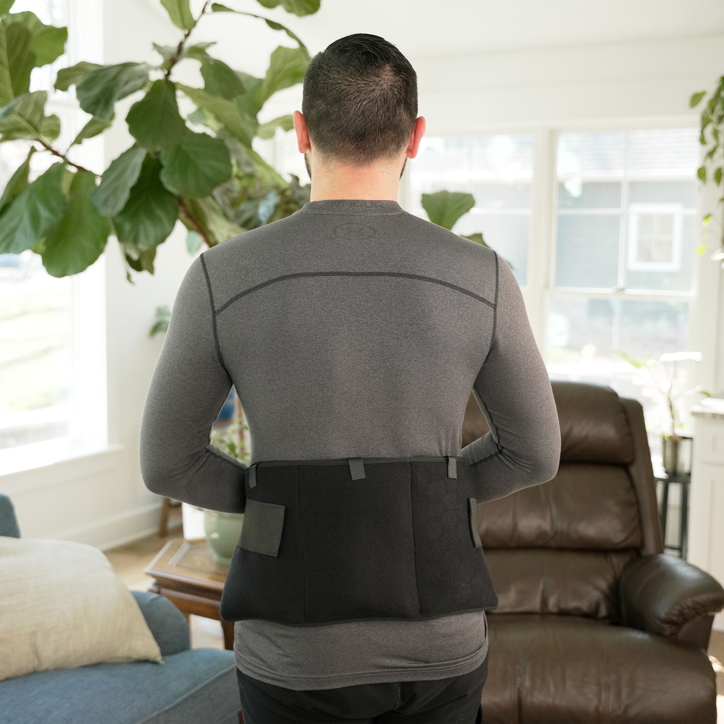 Person wearing a black Soft Ice® Triple Universal Compression Wrap on his lower back in a living room setting