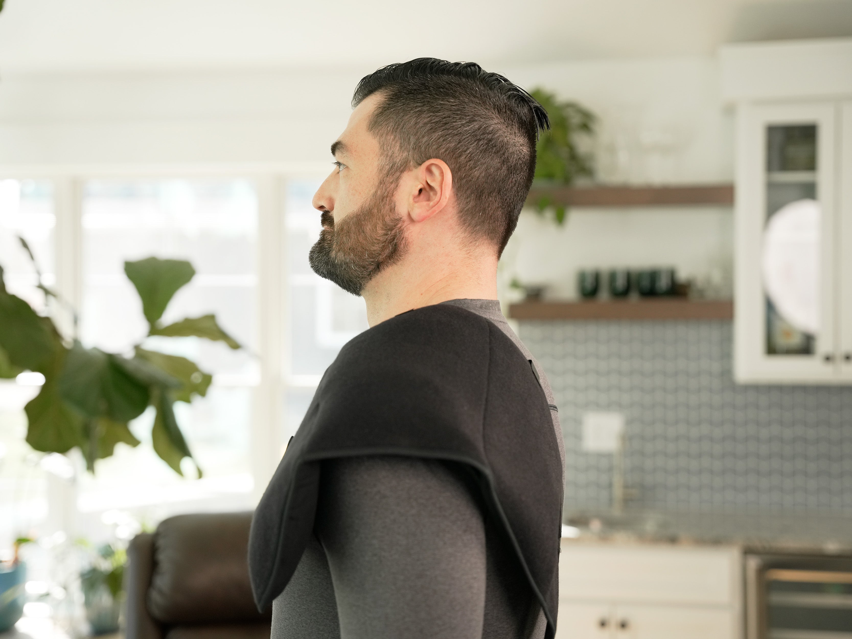 Man standing in a modern kitchen with plants and cabinets in the background wearing a Soft Ice® Triple Universal Compression Wrap on his shoulder