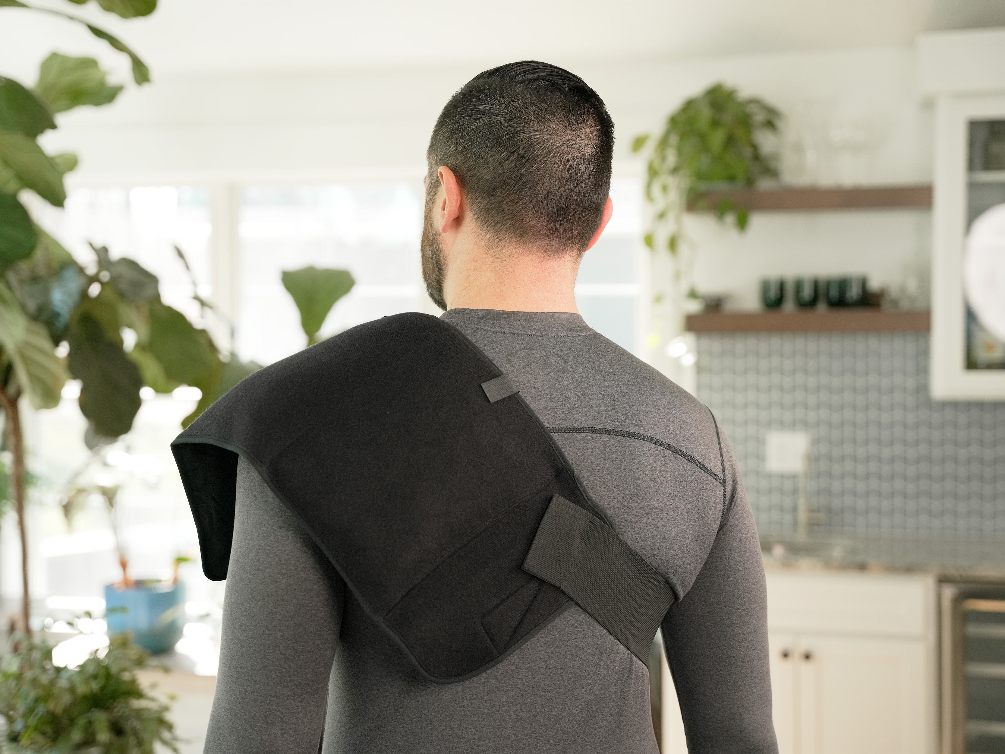 Person wearing a black Soft Ice® Triple Universal Compression Wrap on his shoulder in a kitchen setting