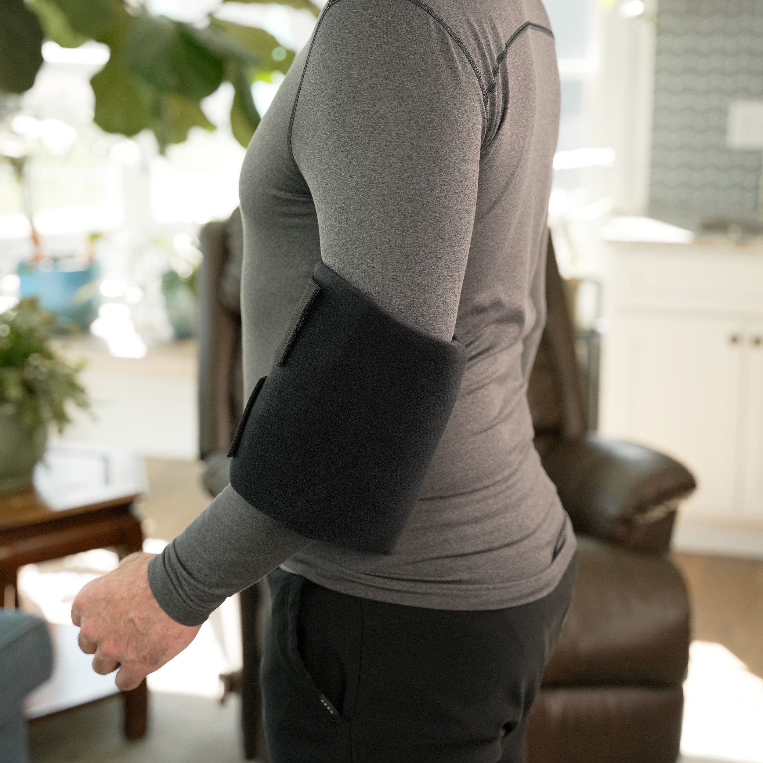 Man wearing a Soft Ice® Large Universal Joint Compression Wrap on his elbow in a living room setting.