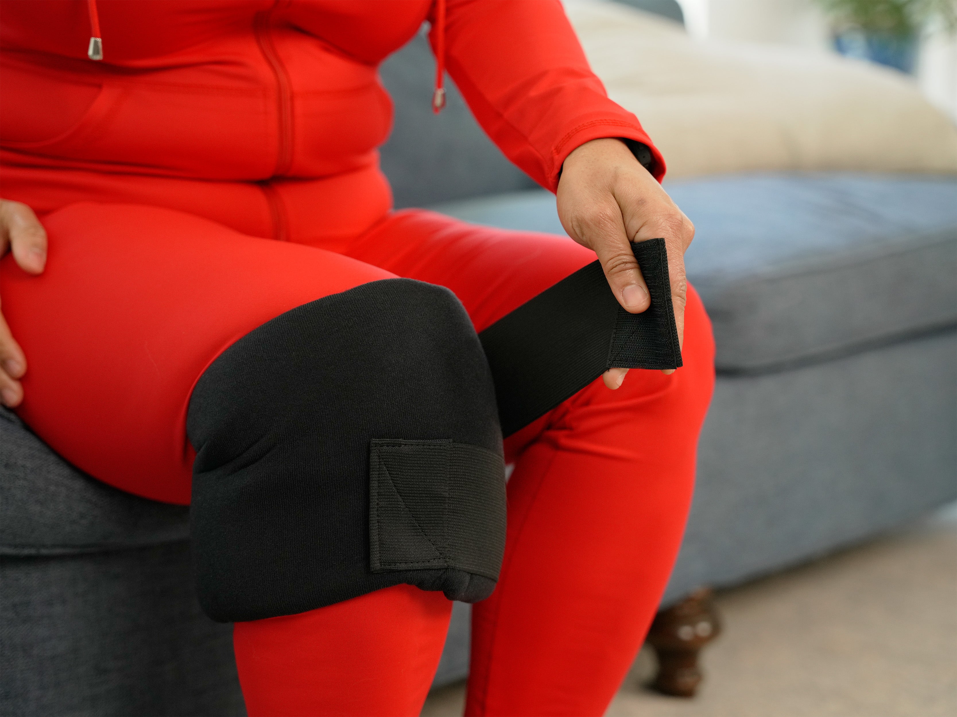 Woman sitting on a couch applying the Soft Ice® Medium Universal Joint Compression Wrap to her knee