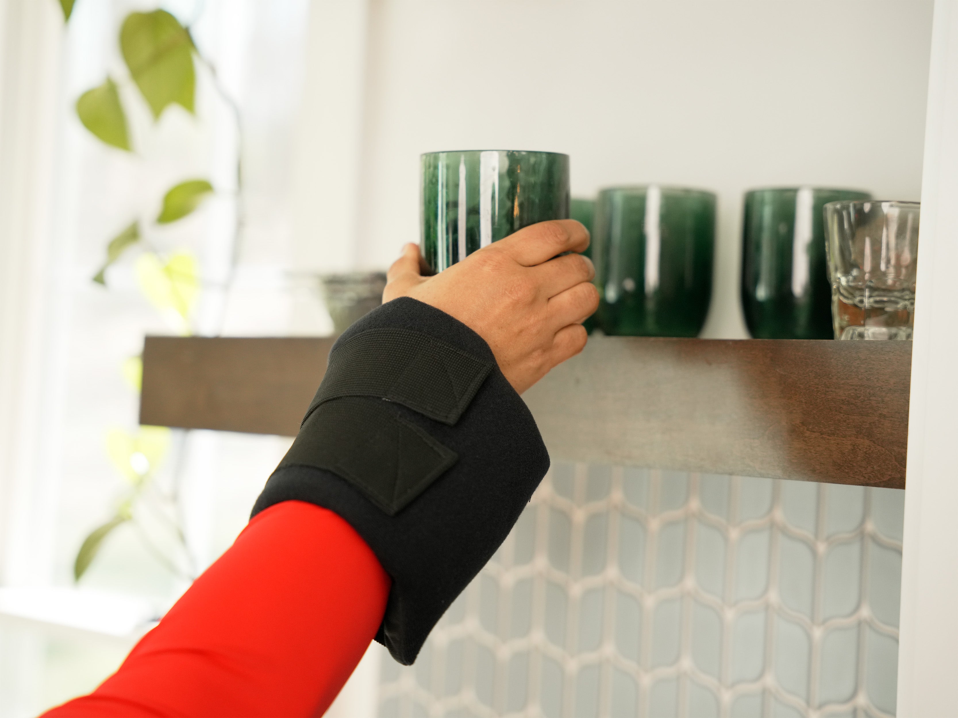 Person with a black Soft Ice® Small Universal Joint Compression Wrap on wrist holding a green mug in a kitchen setting.