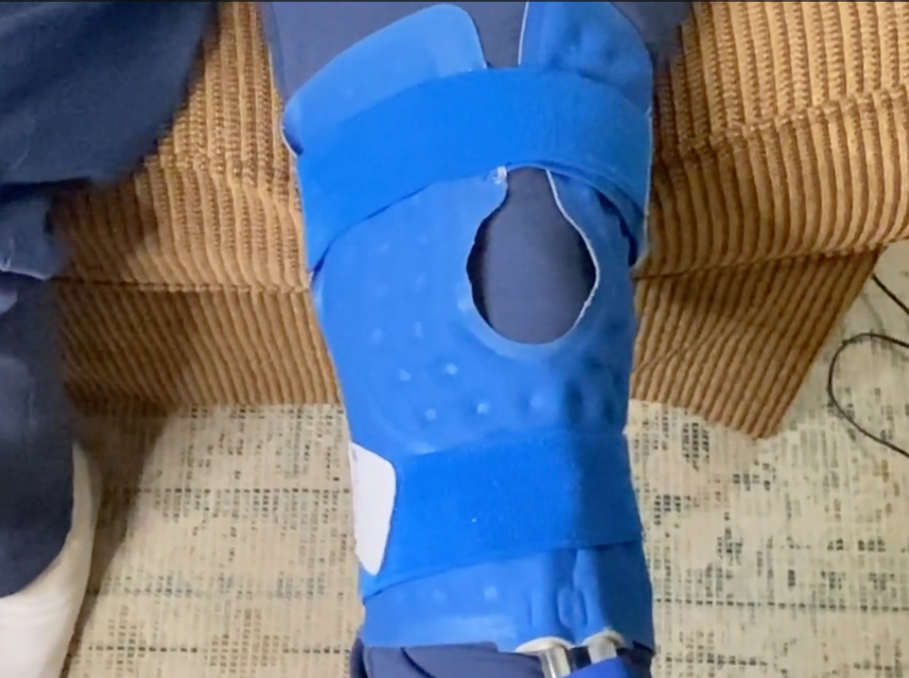 A blue knee & joint Active Ice® Therapy Pad on someones knee that is sitting in a brown chair.