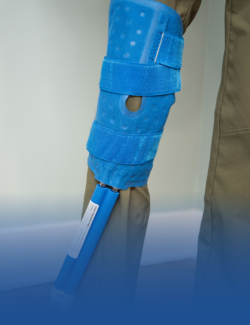 Blue polar active ice® knee & joint therapy pad on someones knee against a wall in a living room setting