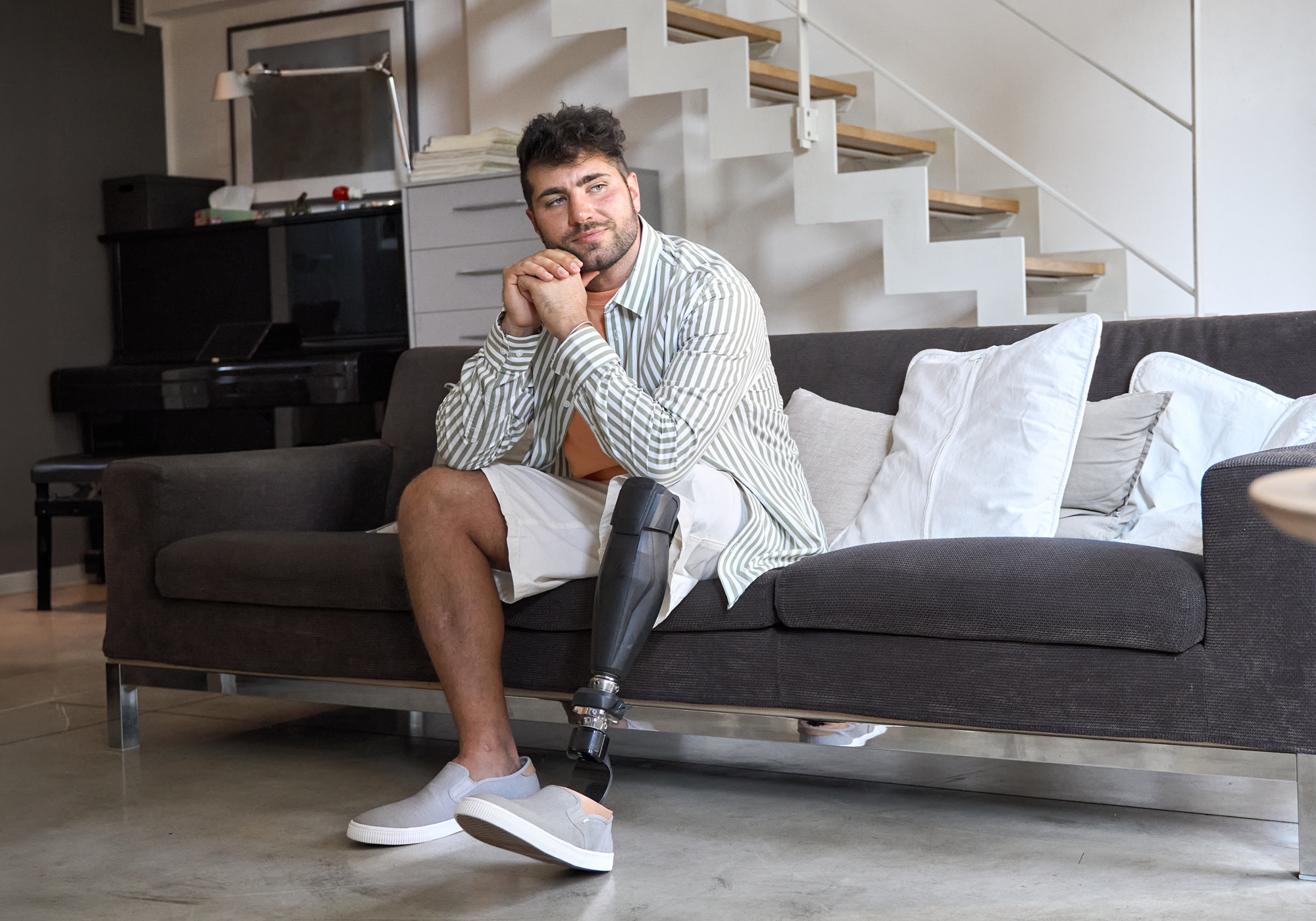 Man with a prosthetic leg sitting on a couch in a modern living room.