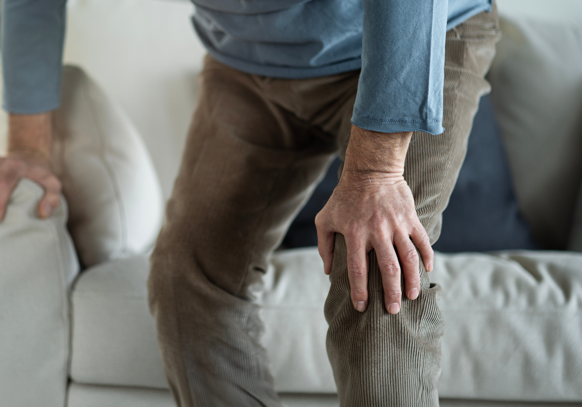 Person having trouble getting off the couch while holding onto it and the other hand holding his knee in pain