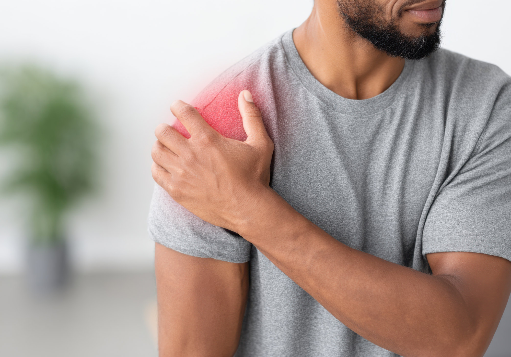 Man in a gray t-shirt holding his shoulder in pain