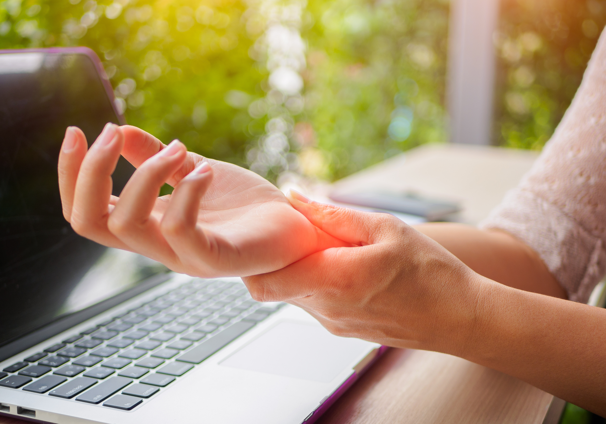 Person with a laptop sitting outside with a closeup of them holding their wrist in pain