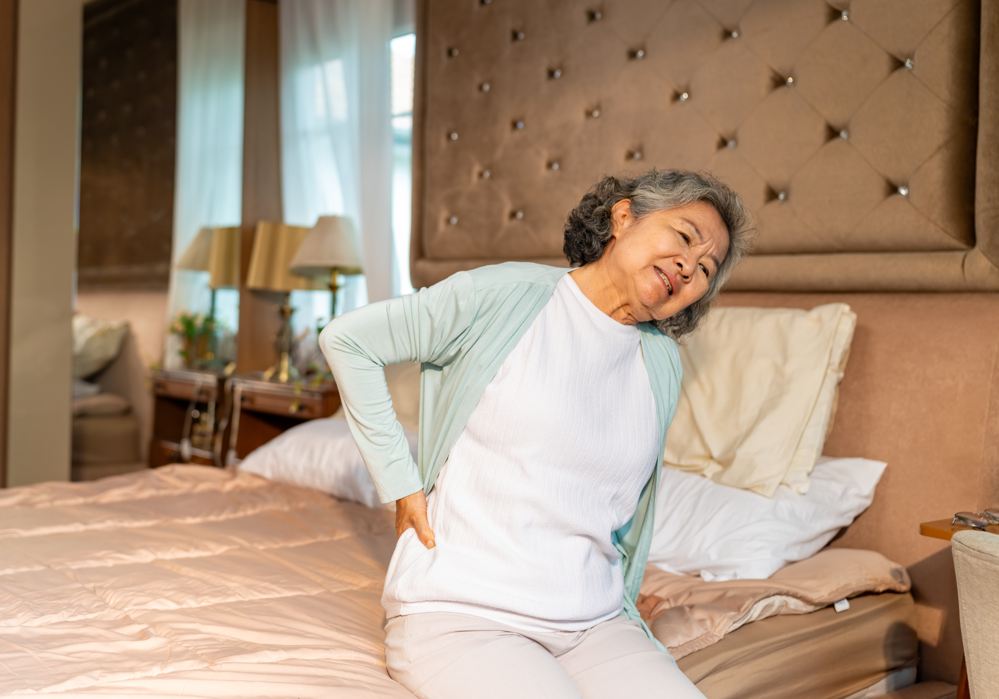 Woman experiencing back pain while trying to get off the bed