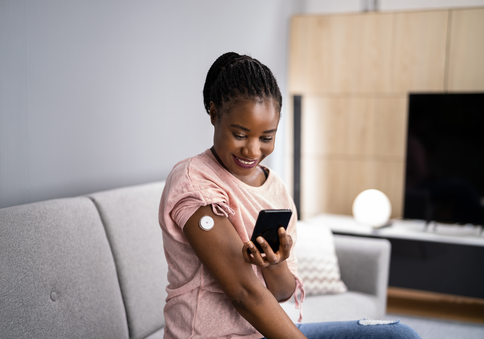 Woman using a smartphone app for diabetes with a bandage on her arm in a living room.