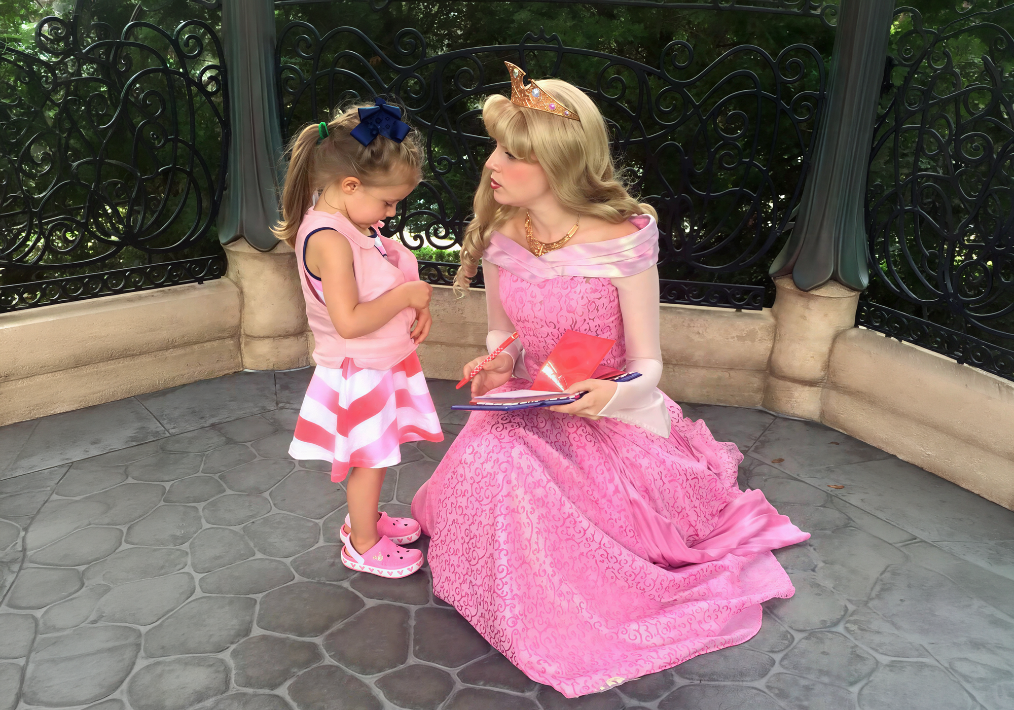 Woman in a pink princess dress interacting with a young girl in a similar dress.