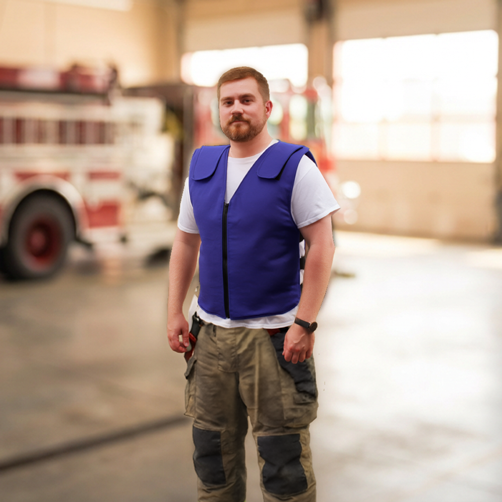 Man wearing a blue flame-resistant cooling vest standing in a garage with a blurred background