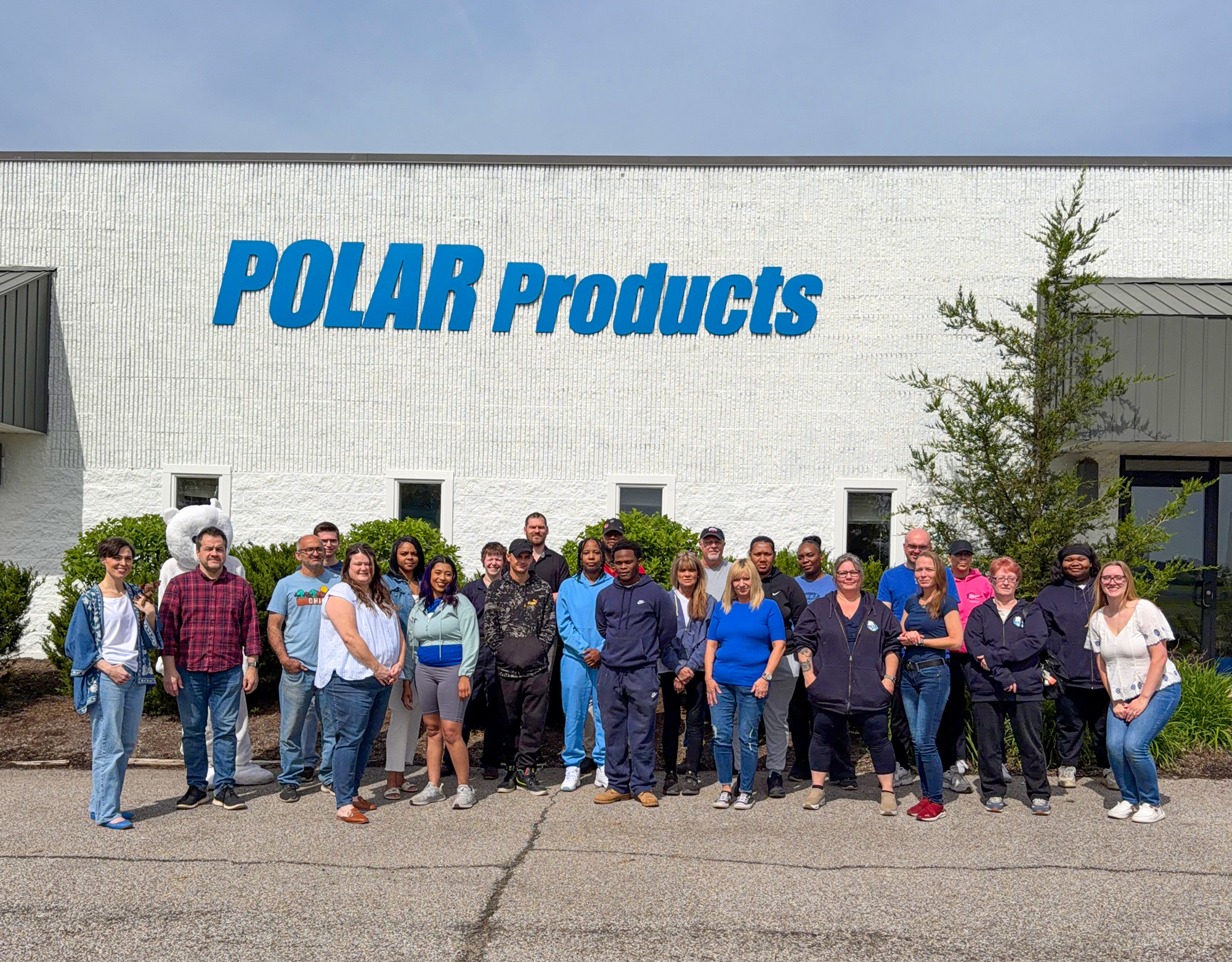 A group of people standing outdoors in front of a white building with large blue 'POLAR Products' signage, photographed during the day under a pale blue sky.