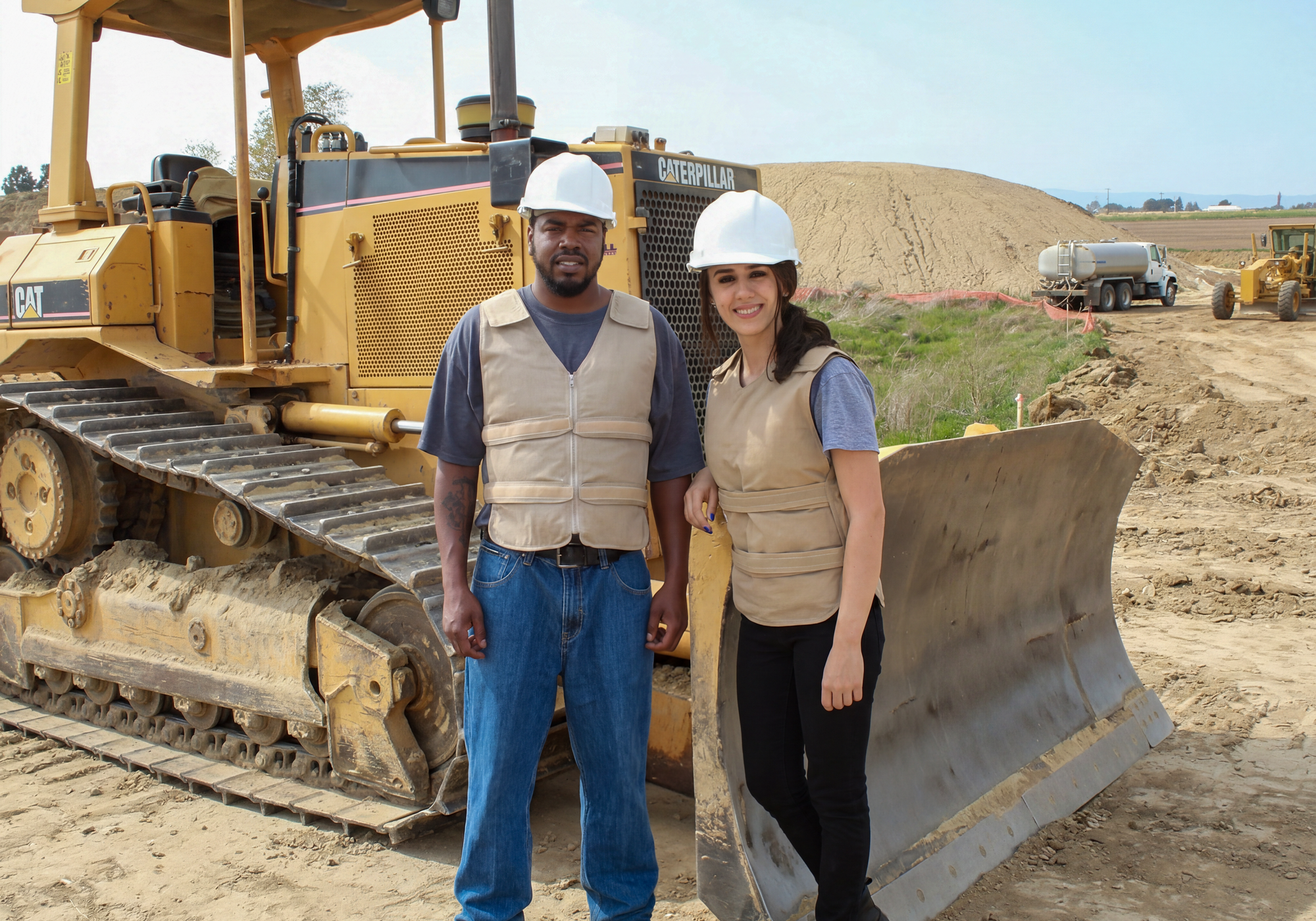 Two people in hard hats standing in front of a large Caterpillar bulldozer on a construction site.