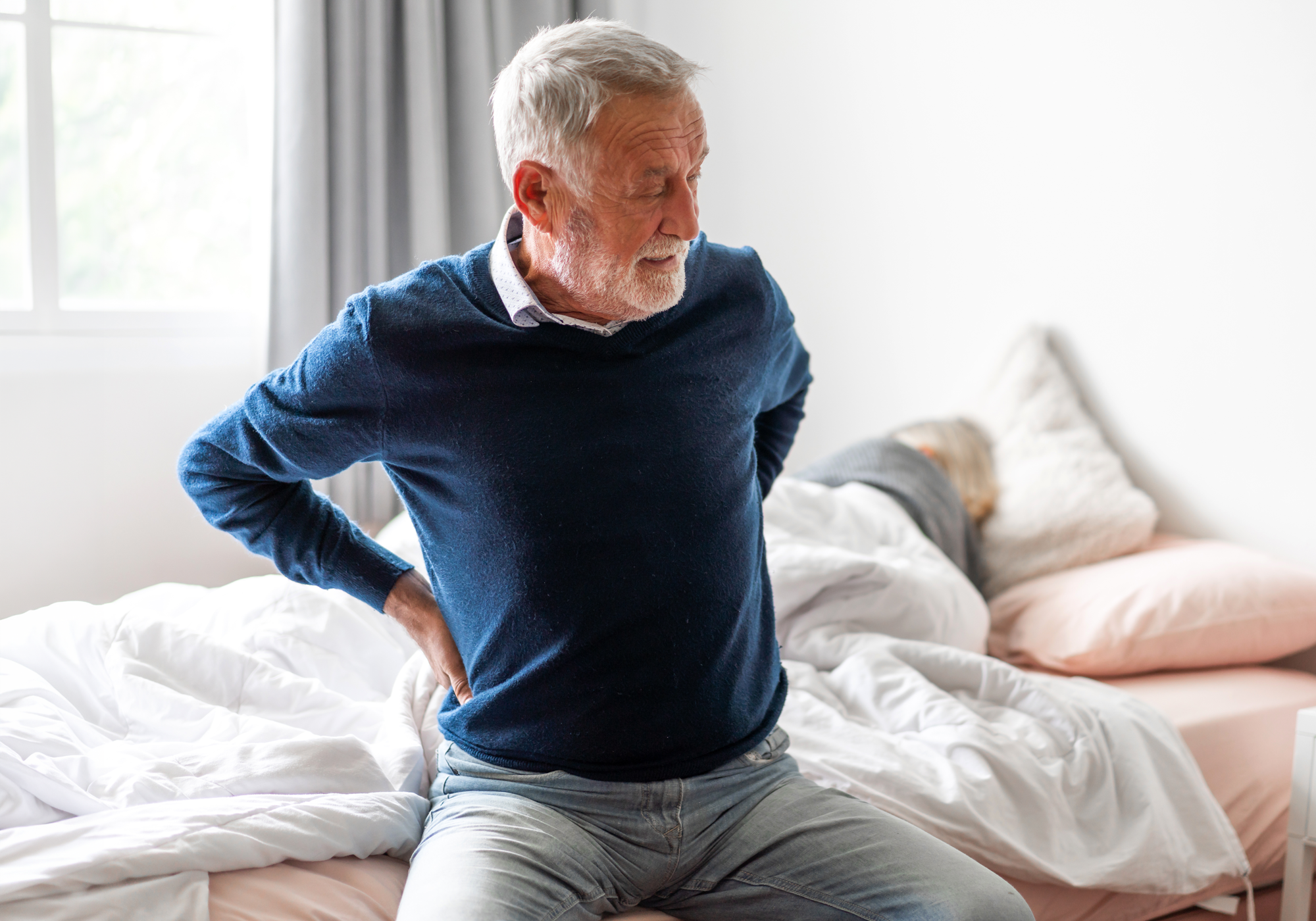 Senior man experiencing back pain in a bedroom setting.
