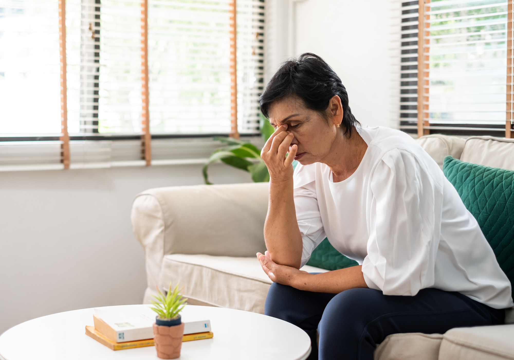 Woman sitting on a couch with a concerned expression, holding her head.