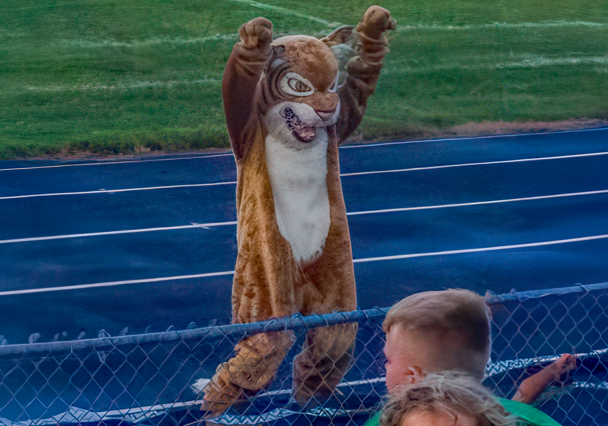 Person in a squirrel mascot costume standing on a blue track with grass in the background