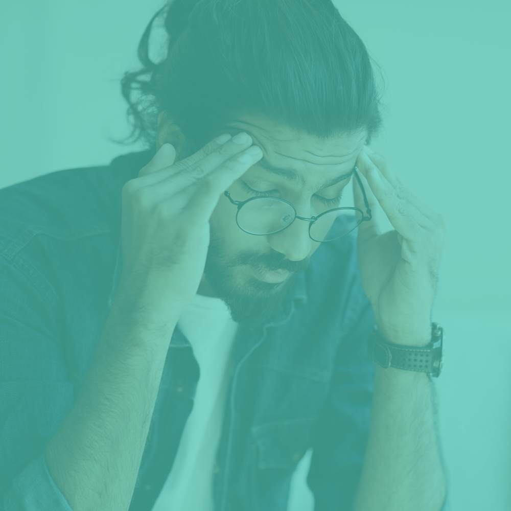 Person with glasses holding their head, experiencing discomfort, with a teal filter applied.