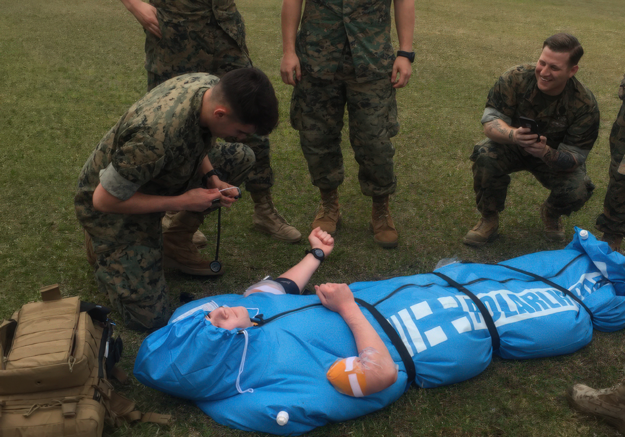 Military training exercise with soldiers around a person on a blue stretcher