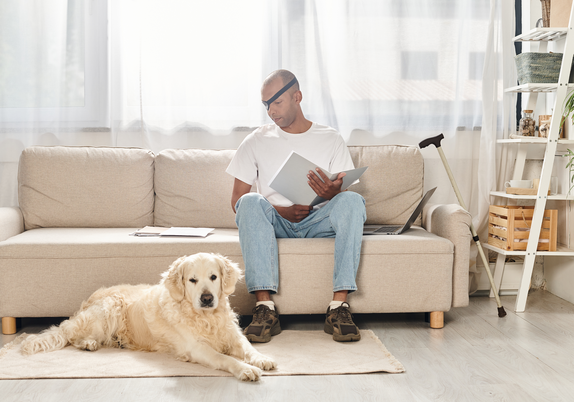 Man sitting on a couch with a dog in a living room wearing an eyepatch and cane propped up against the couch.