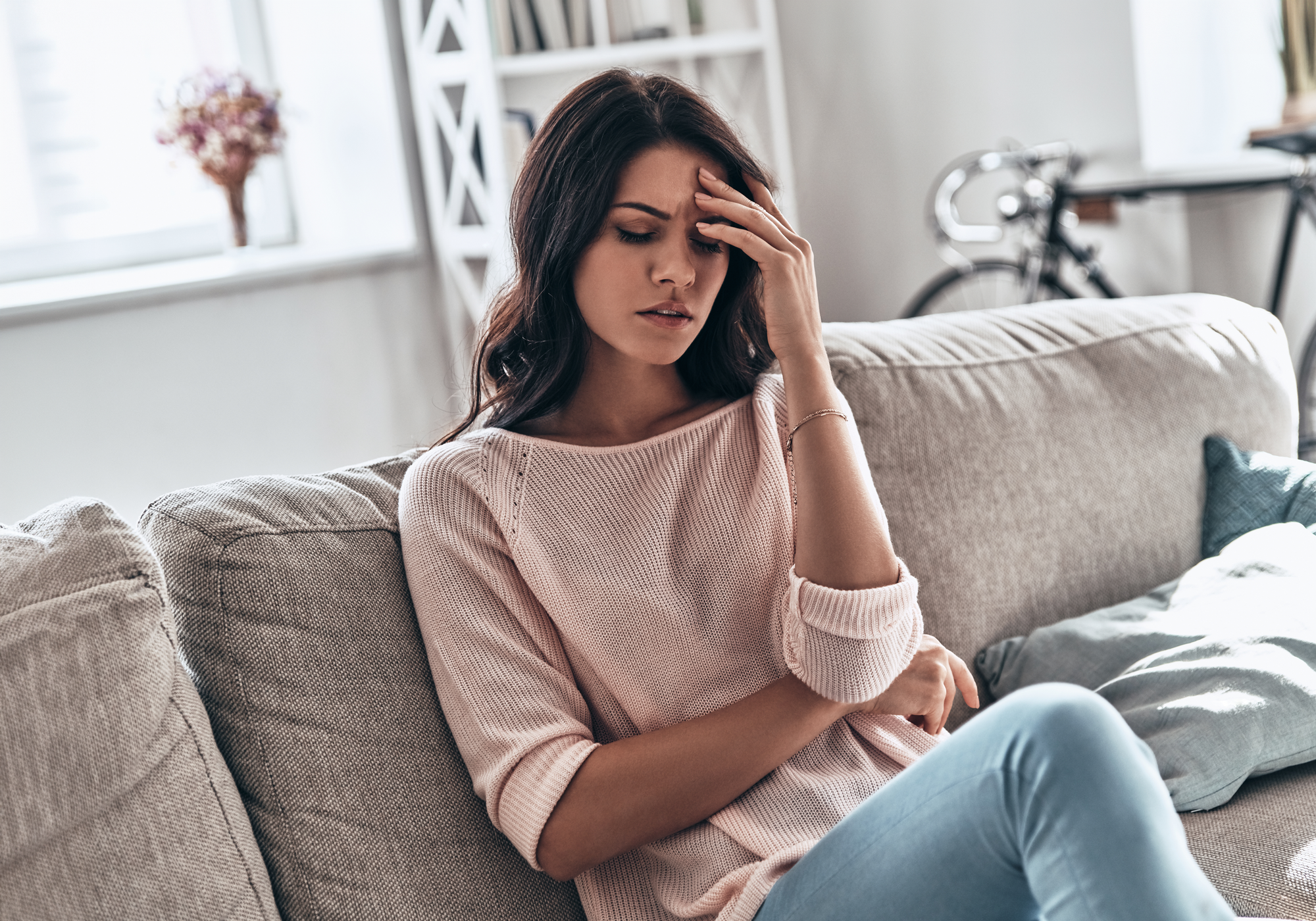 Woman sitting on a couch with a concerned expression, holding her head.